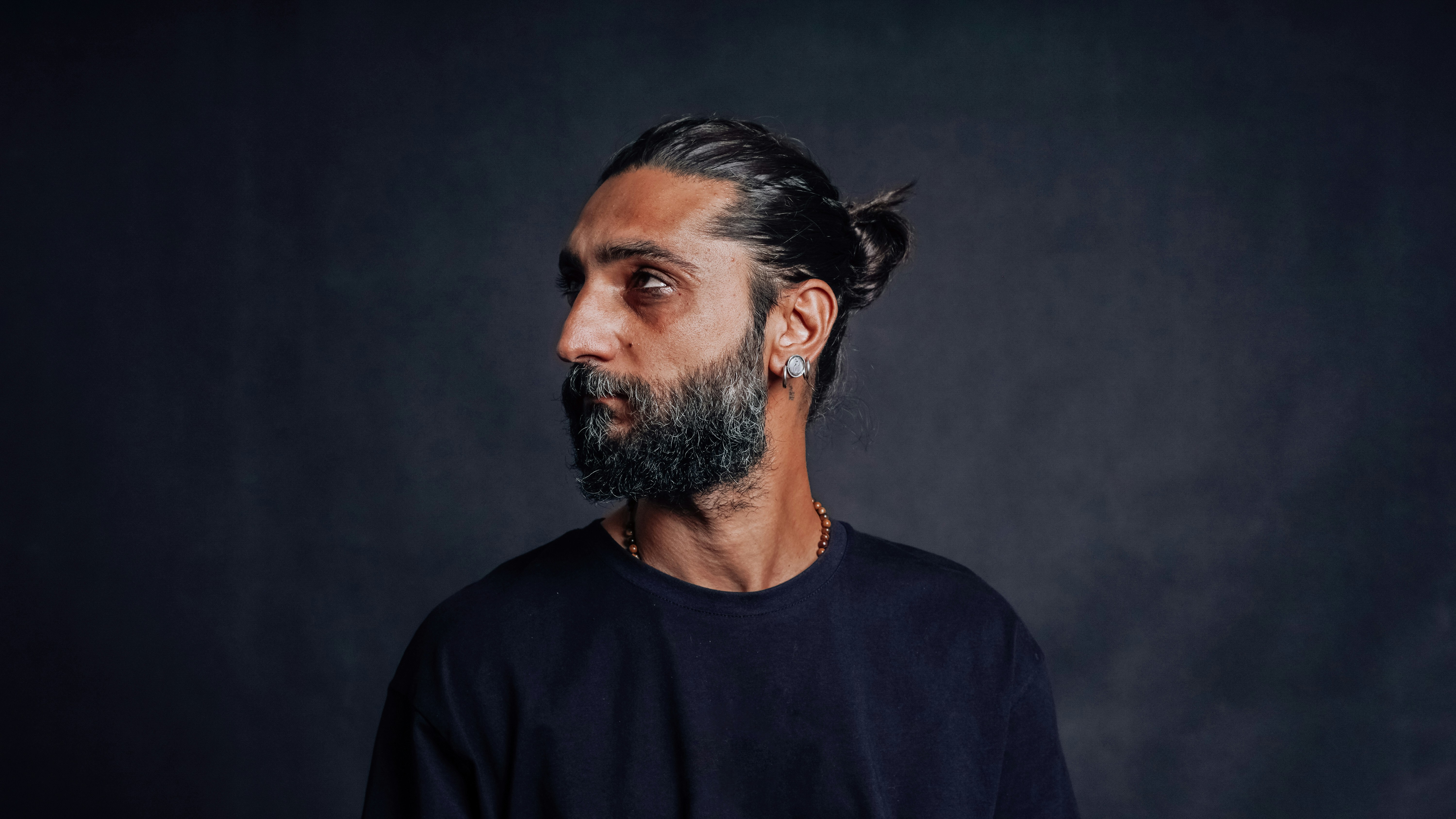 A high-resolution portrait of a bearded man wearing a casual t-shirt and a single earring