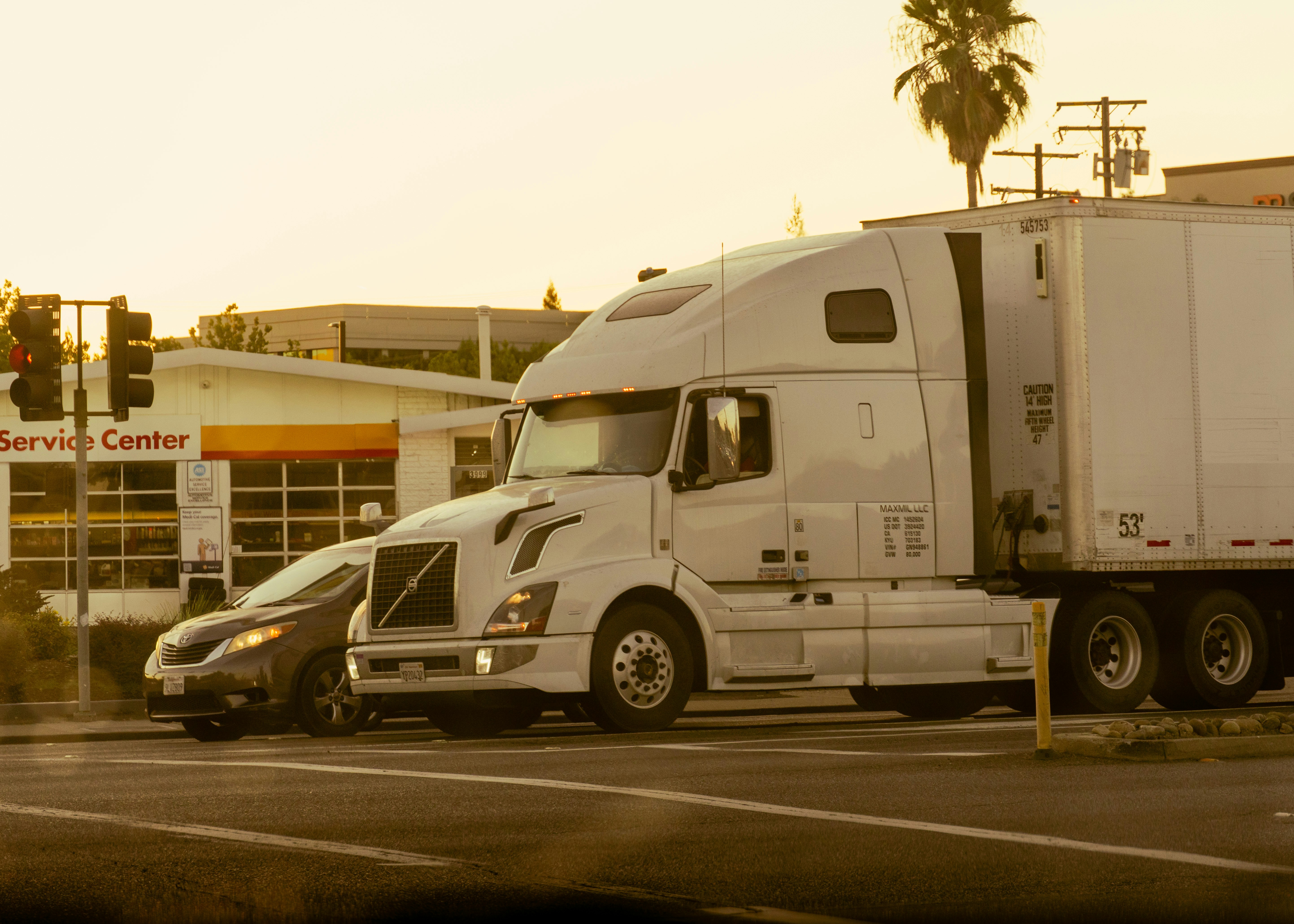 A semi-truck crosses a road next to a car.