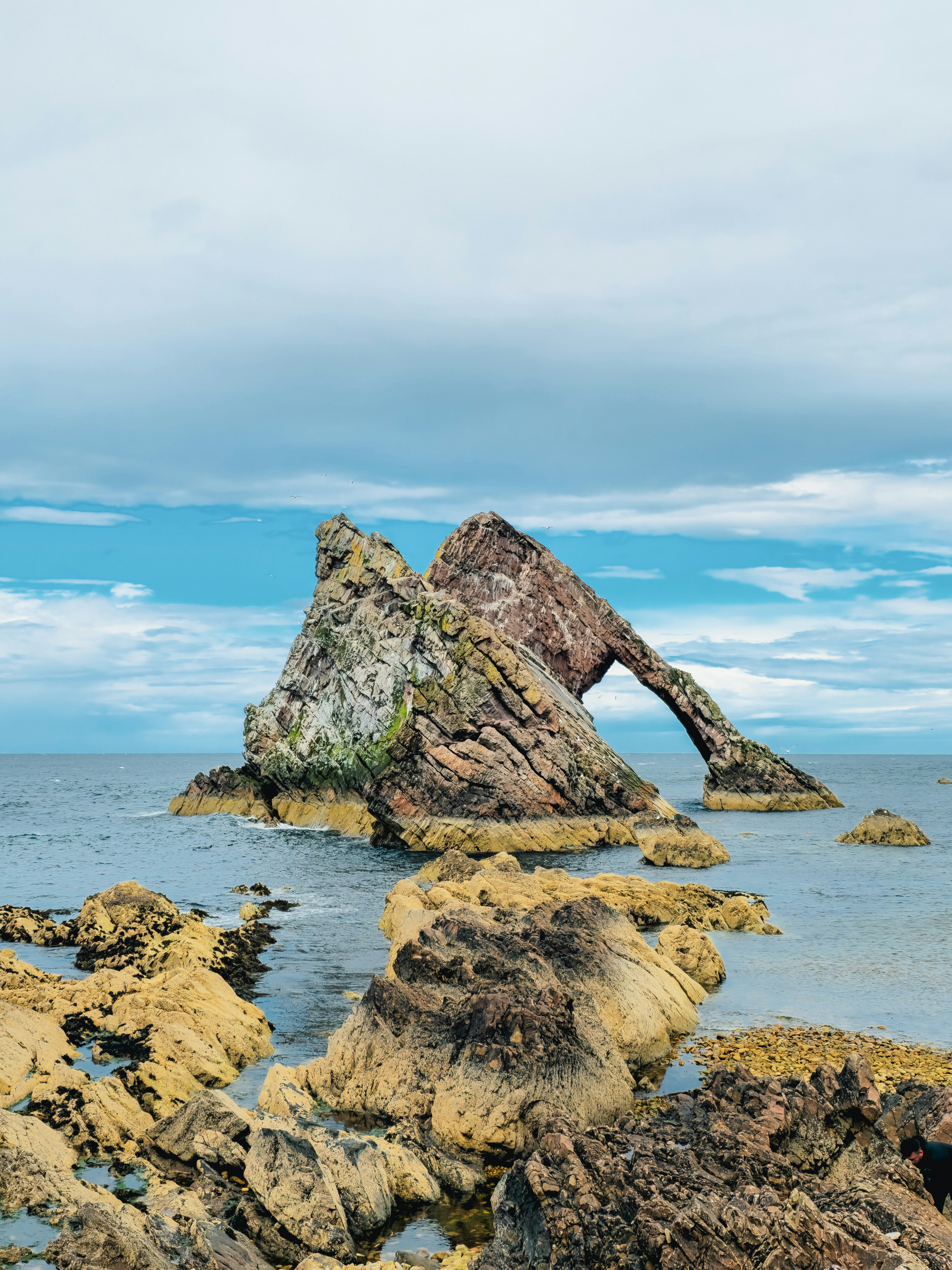 A sea arch and rocks under a cloudy sky.