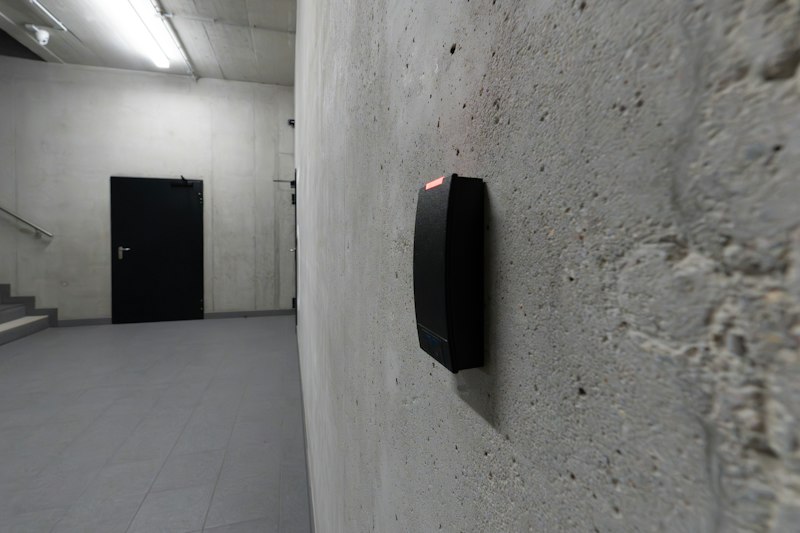A black access-card reader on a concrete wall beside a closed door