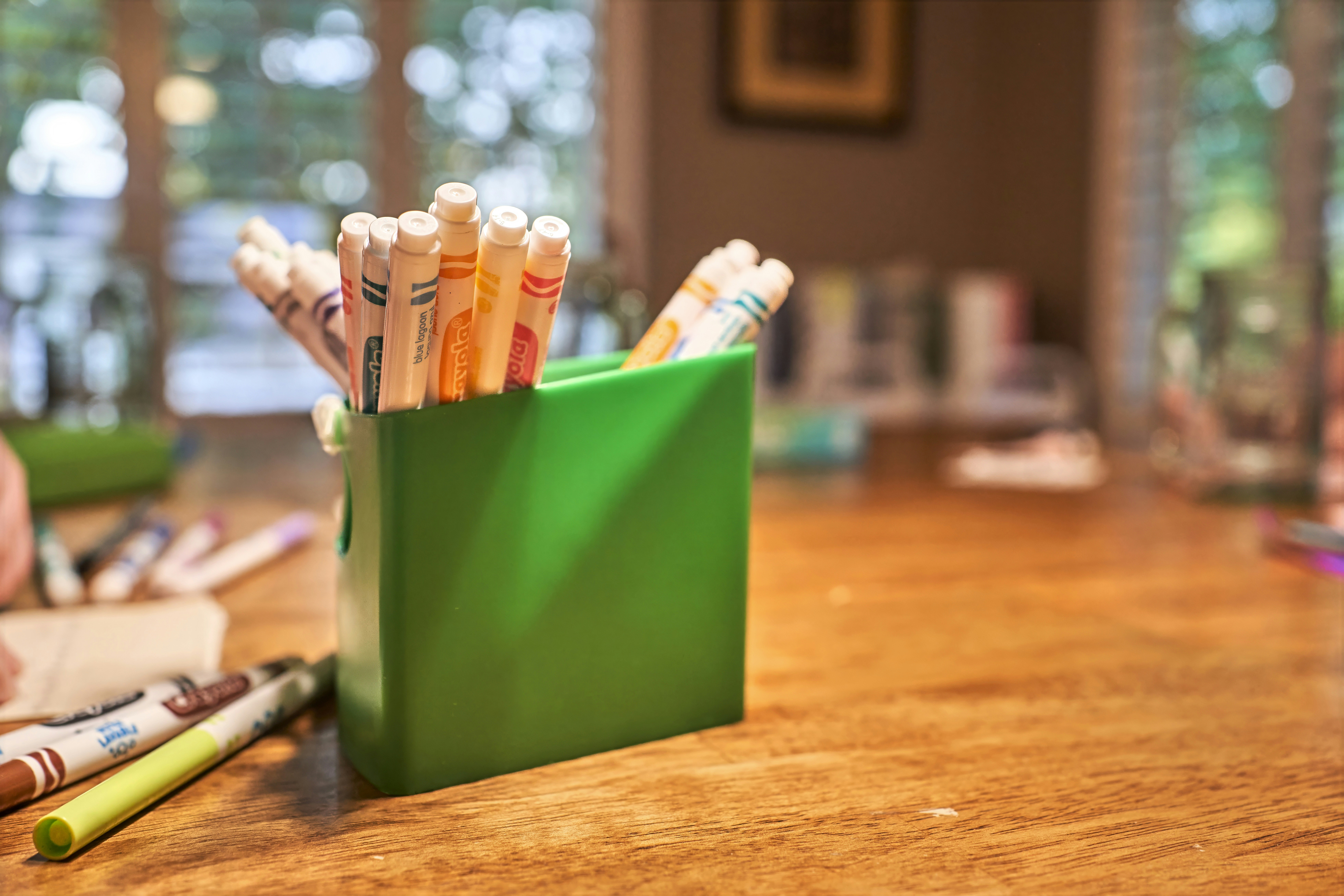 Crayons are held in a green box on a table.