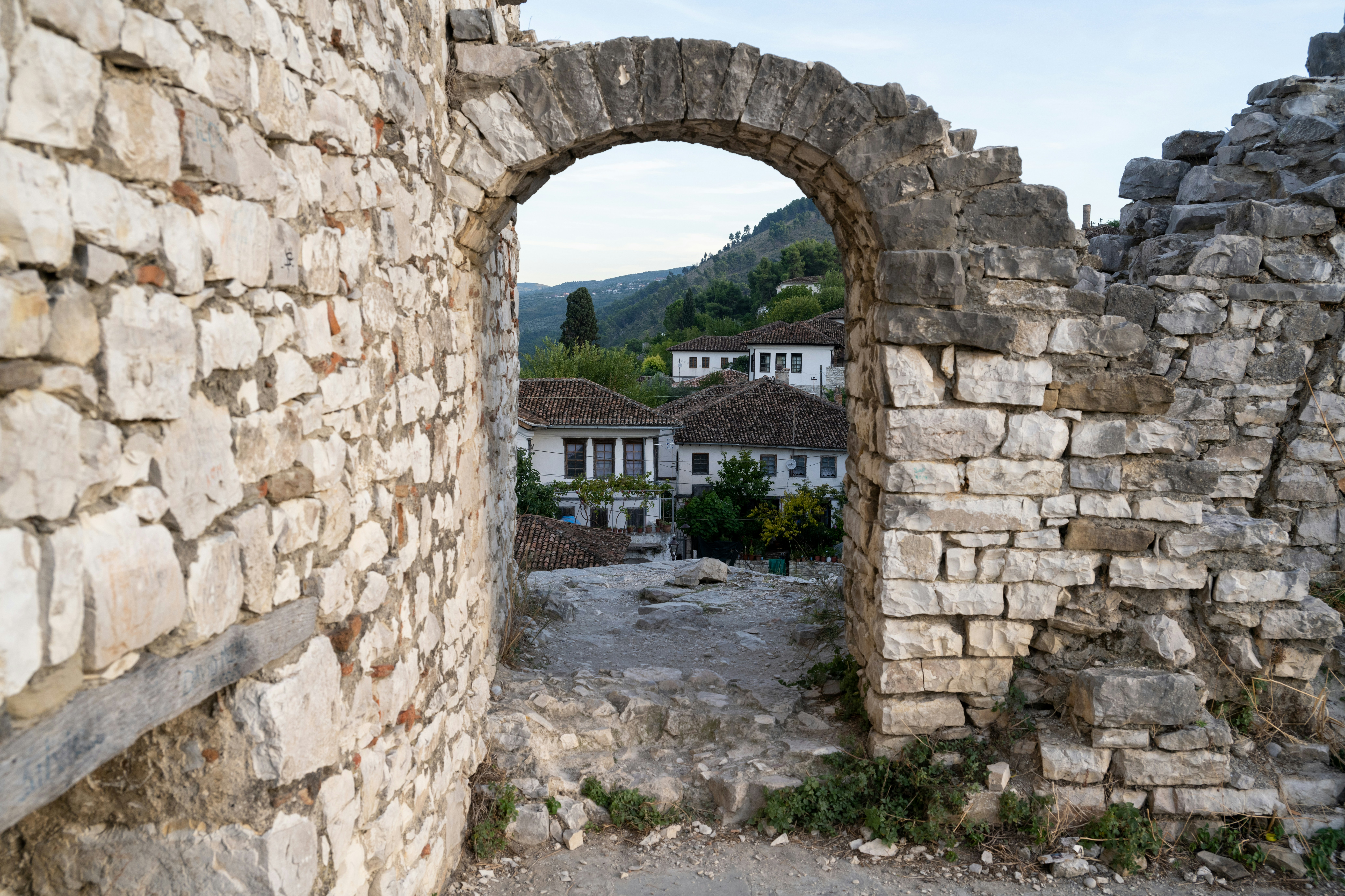 Stone archway reveals houses and a hilly landscape.