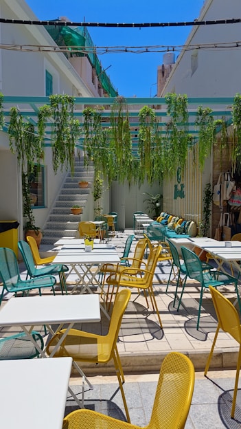 Outdoor restaurant with white tables and colorful chairs.