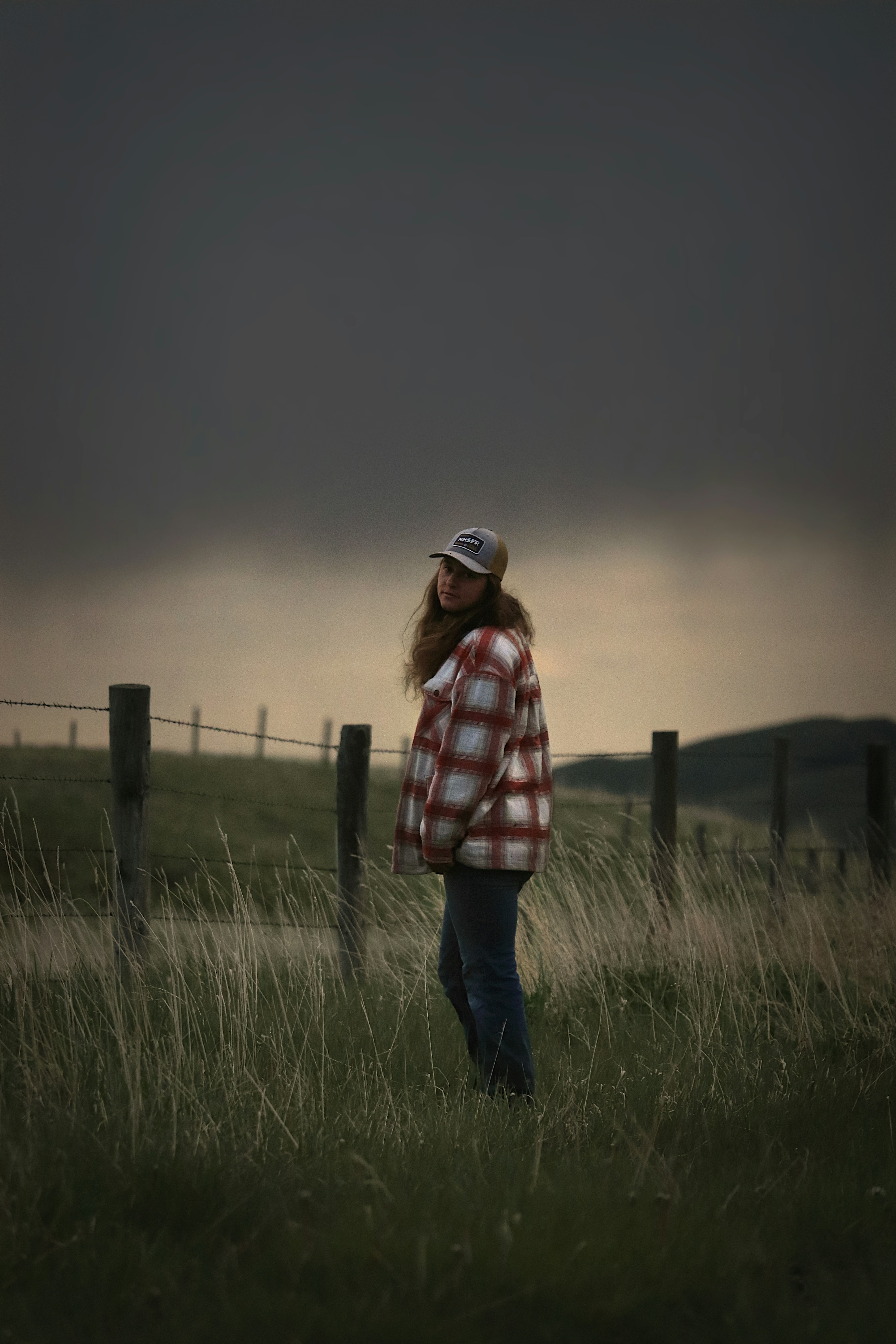 Woman stands in a field with dark, stormy skies.