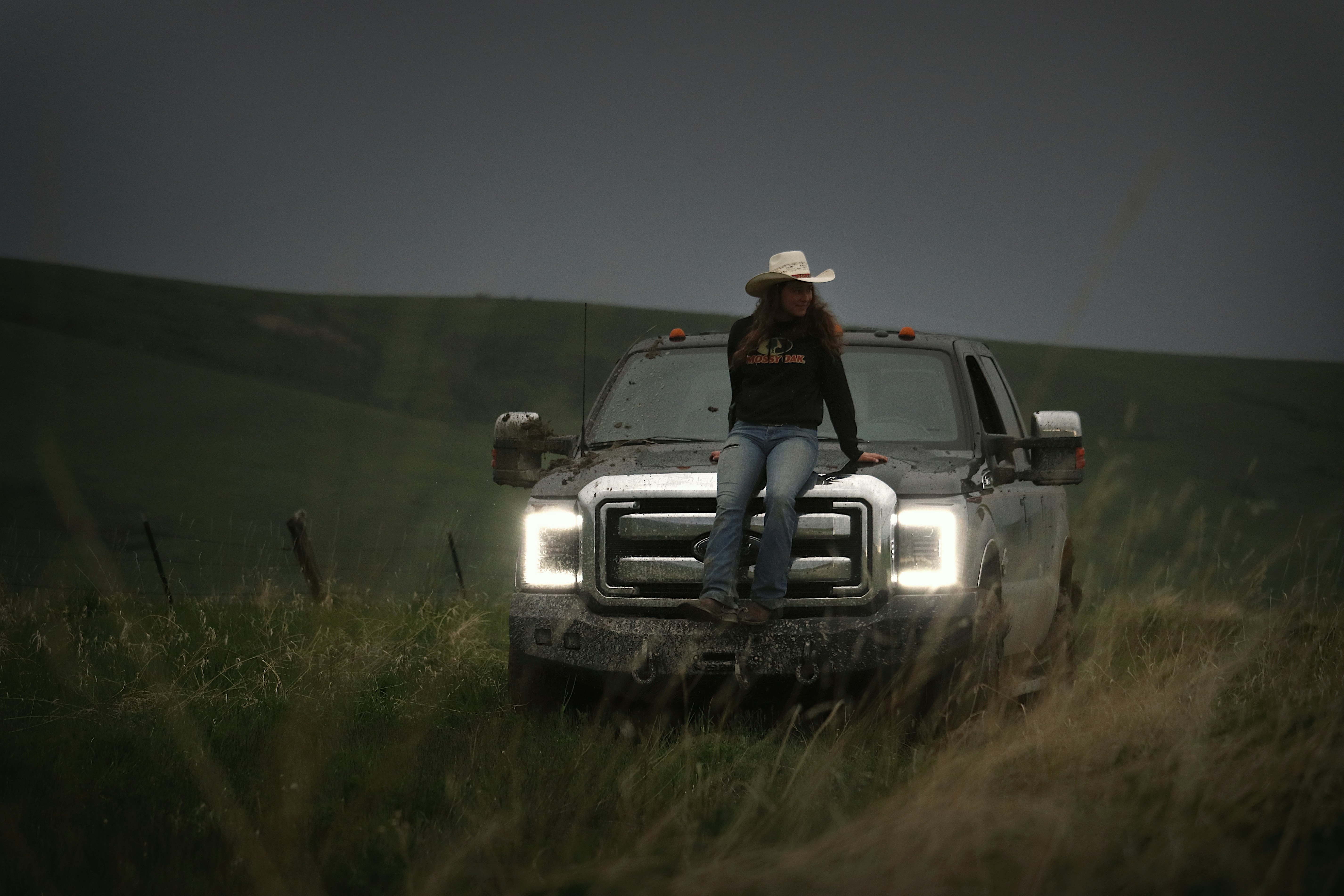 Cowgirl sits on a truck in a field.
