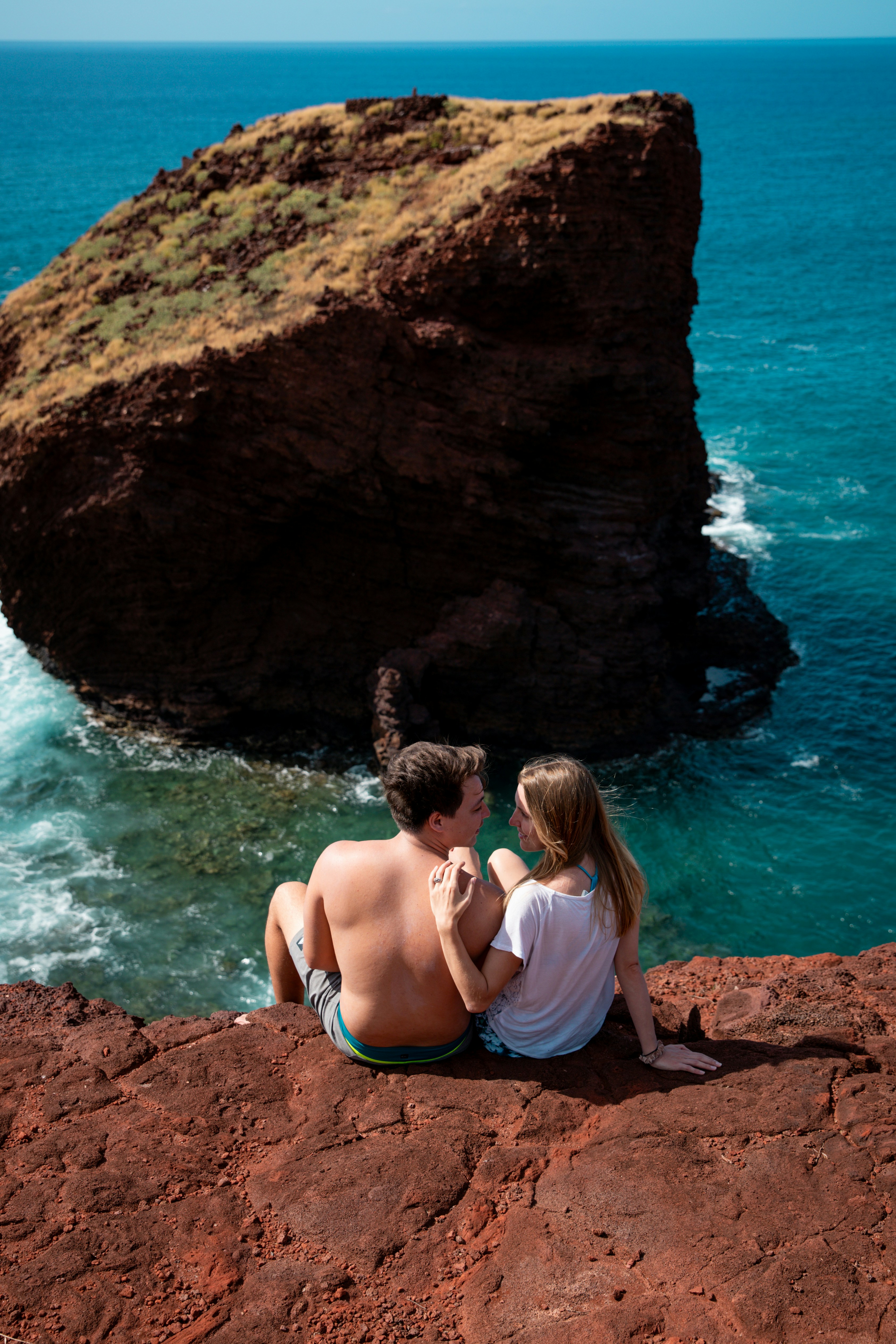 Couple sitting on cliff overlooking ocean and rock
