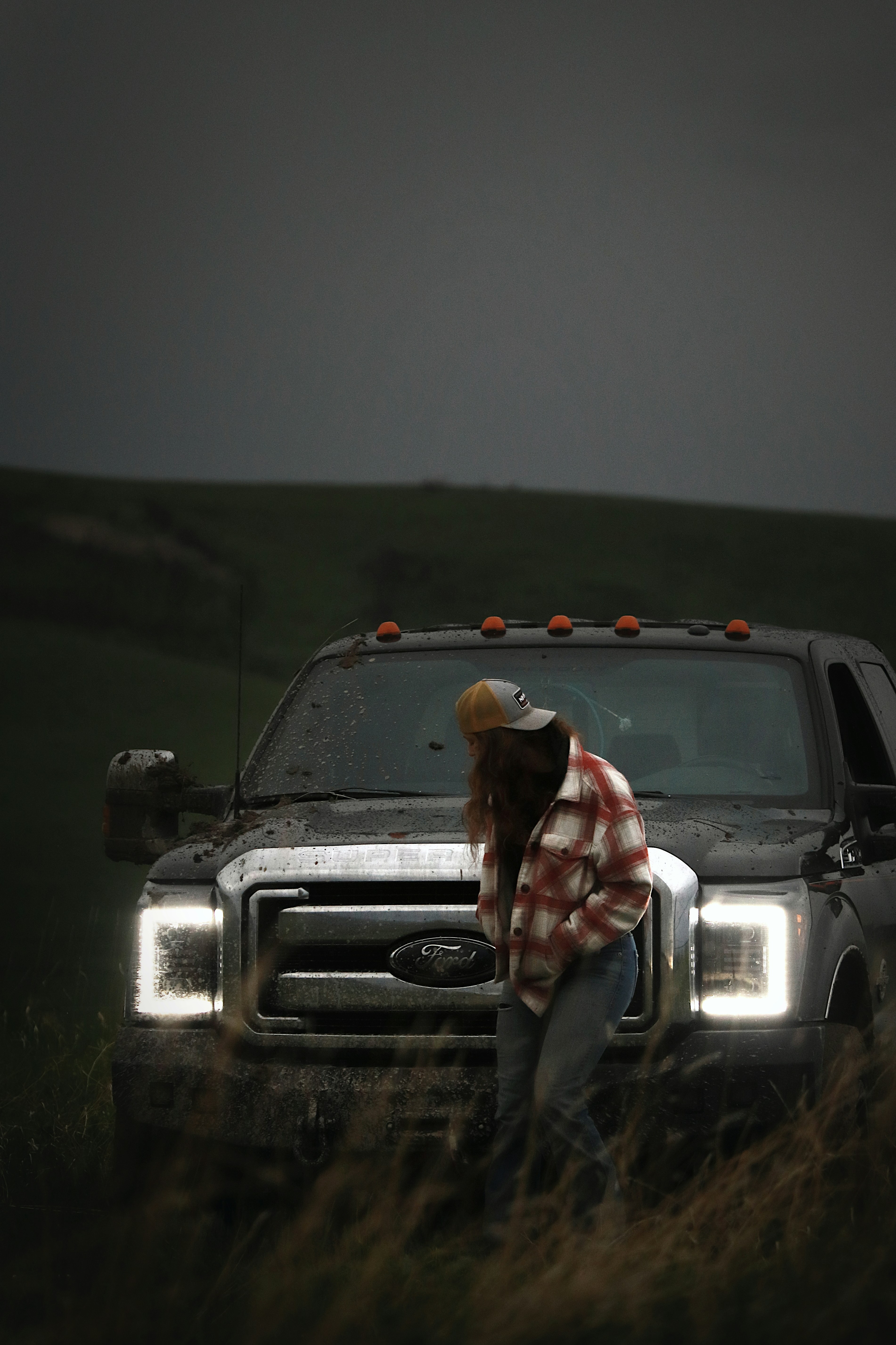 A person stands by a dirty truck in a field.