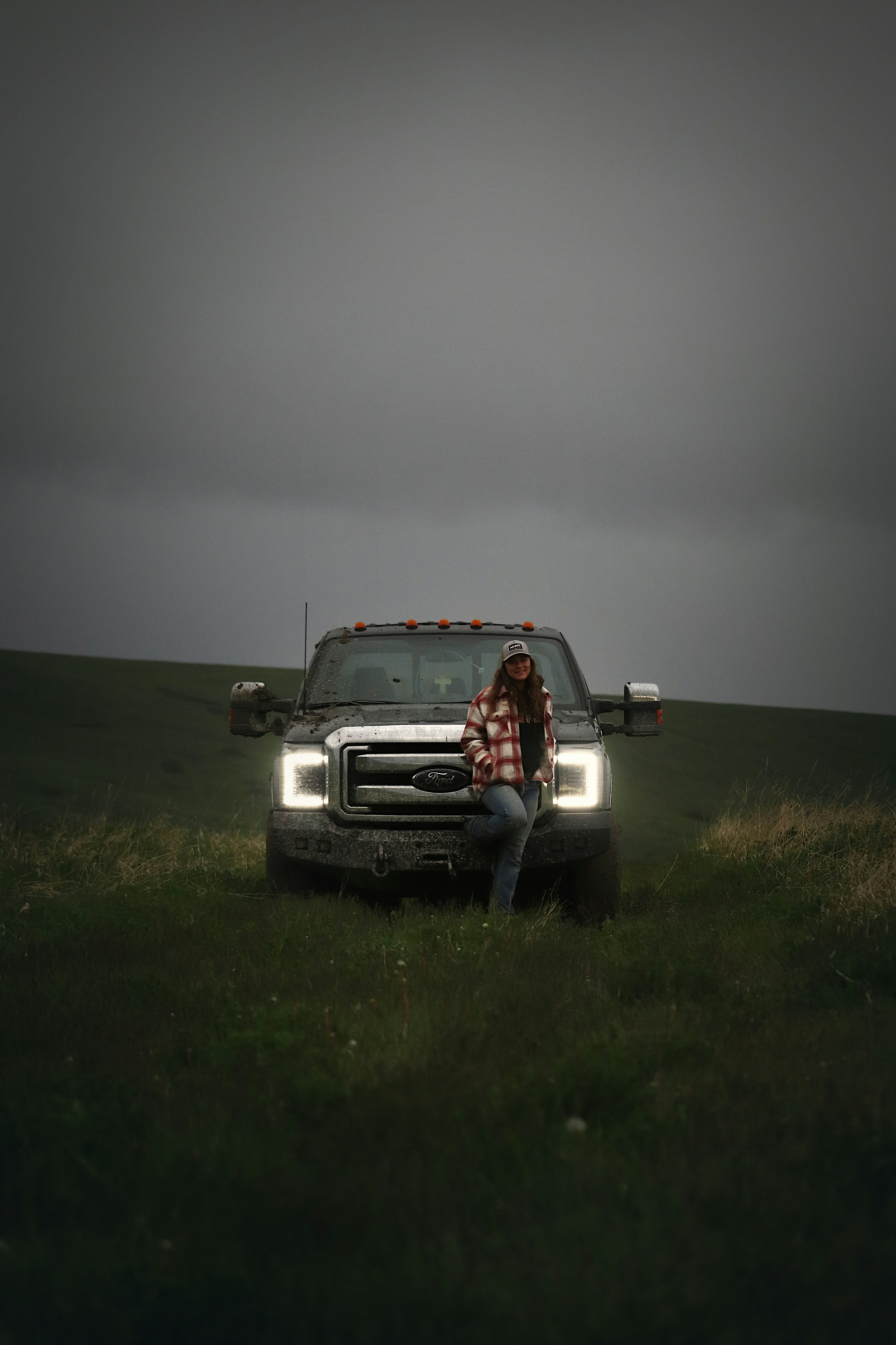 A woman leans on a truck under a dark sky.