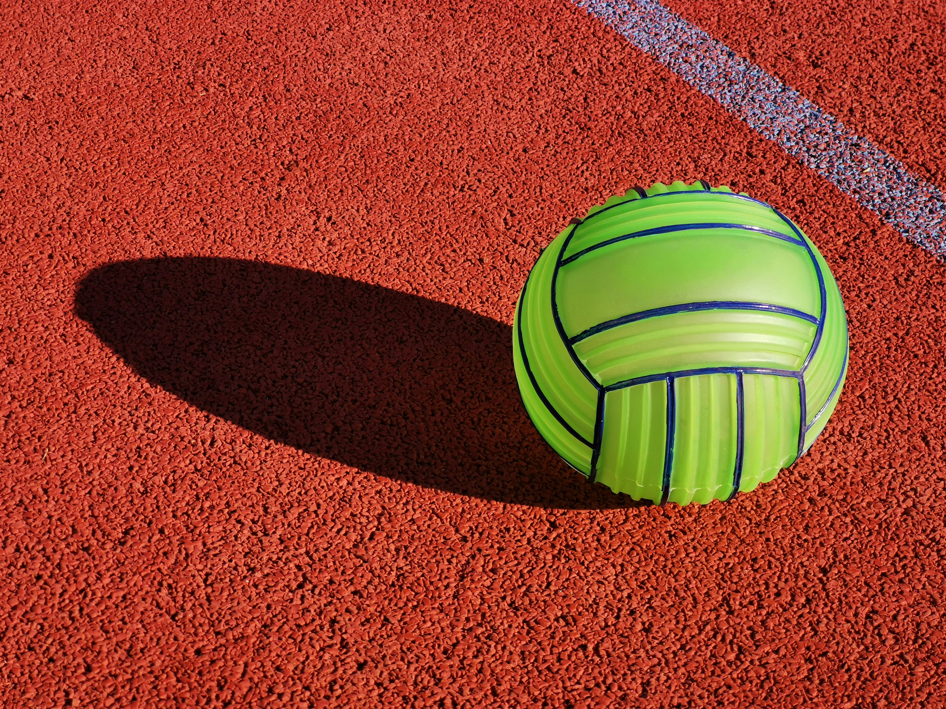 A green volleyball sits on red ground.