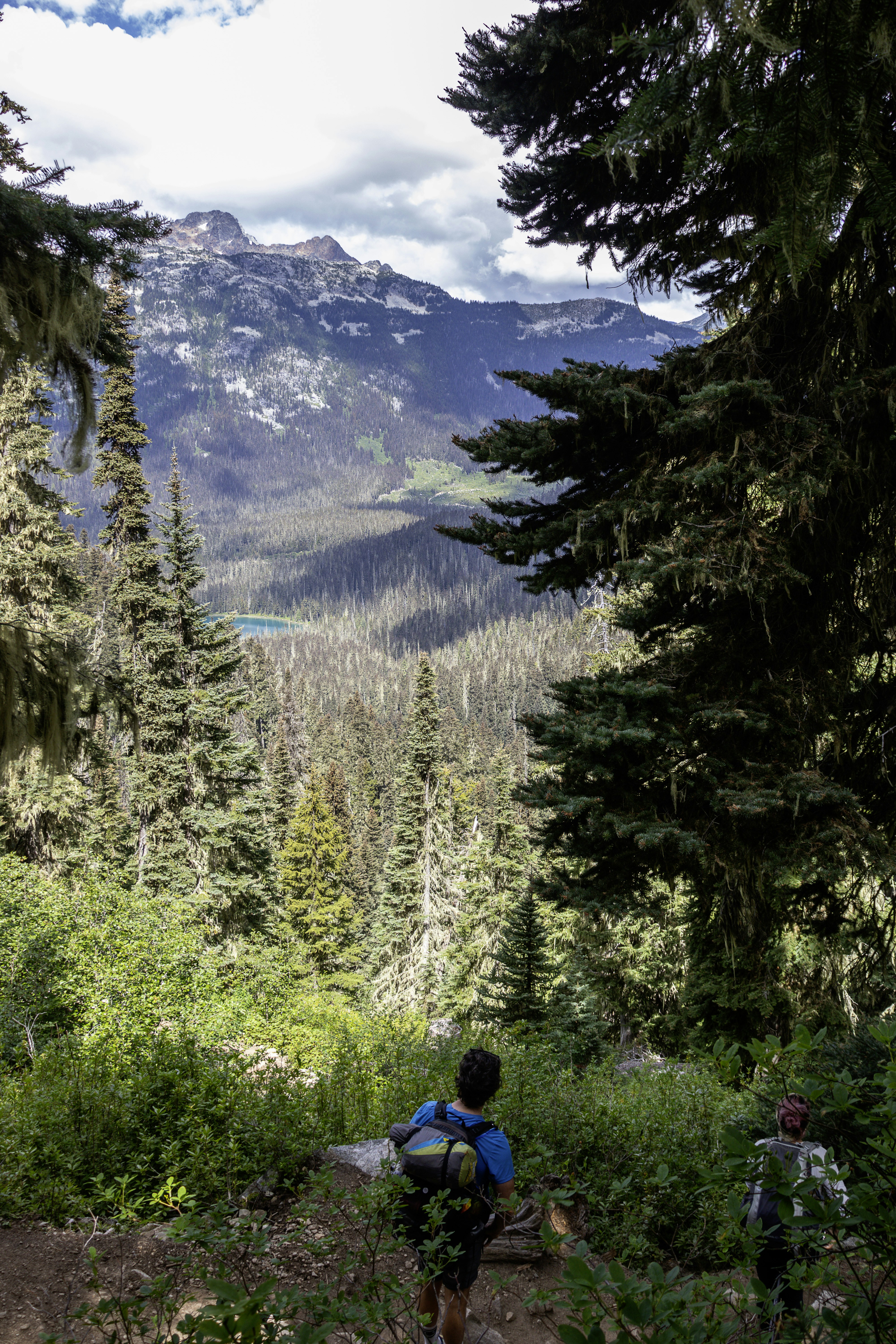 Hikers descend a trail overlooking mountain scenery.