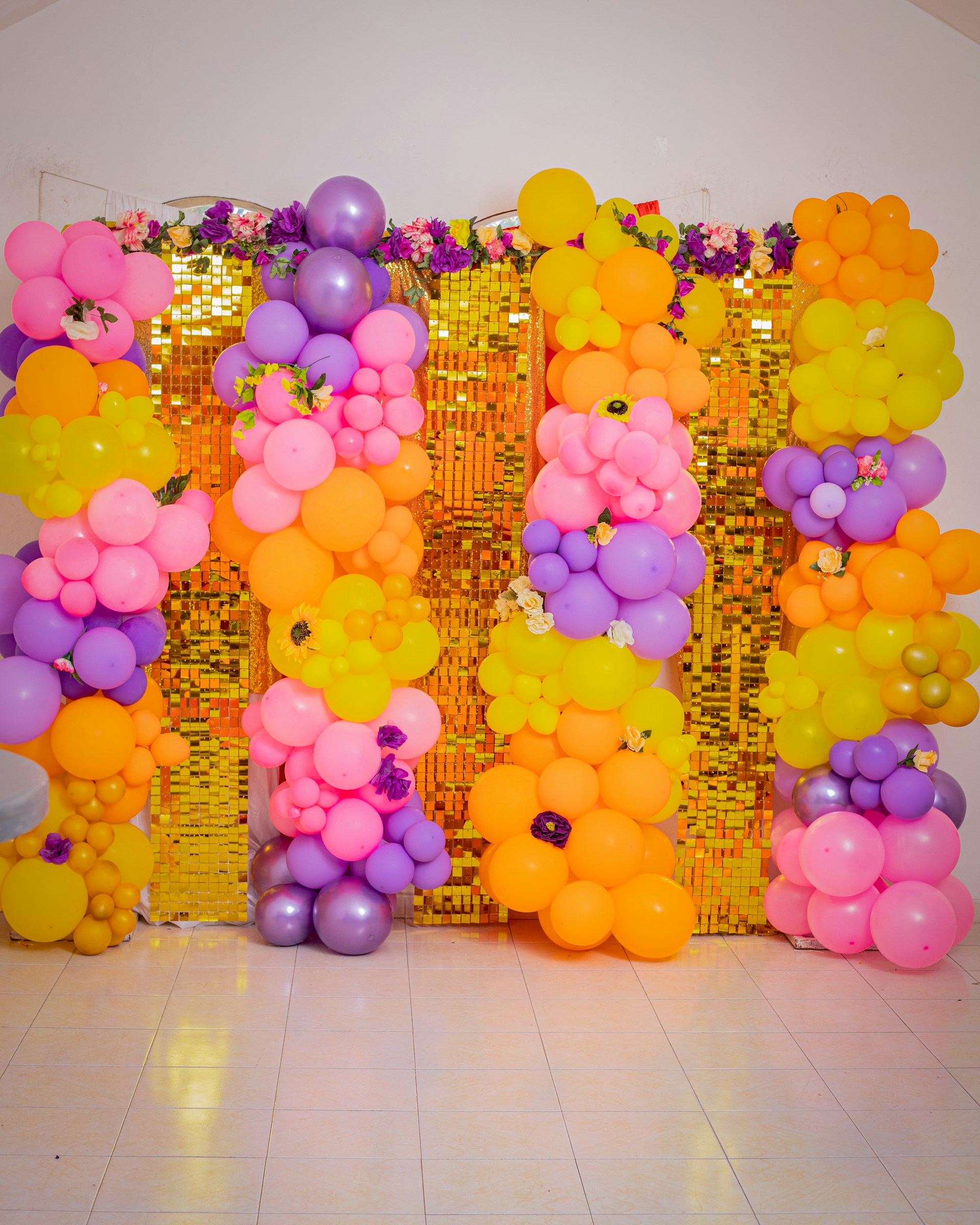 Colorful balloon arrangements decorate a sparkly, golden backdrop.