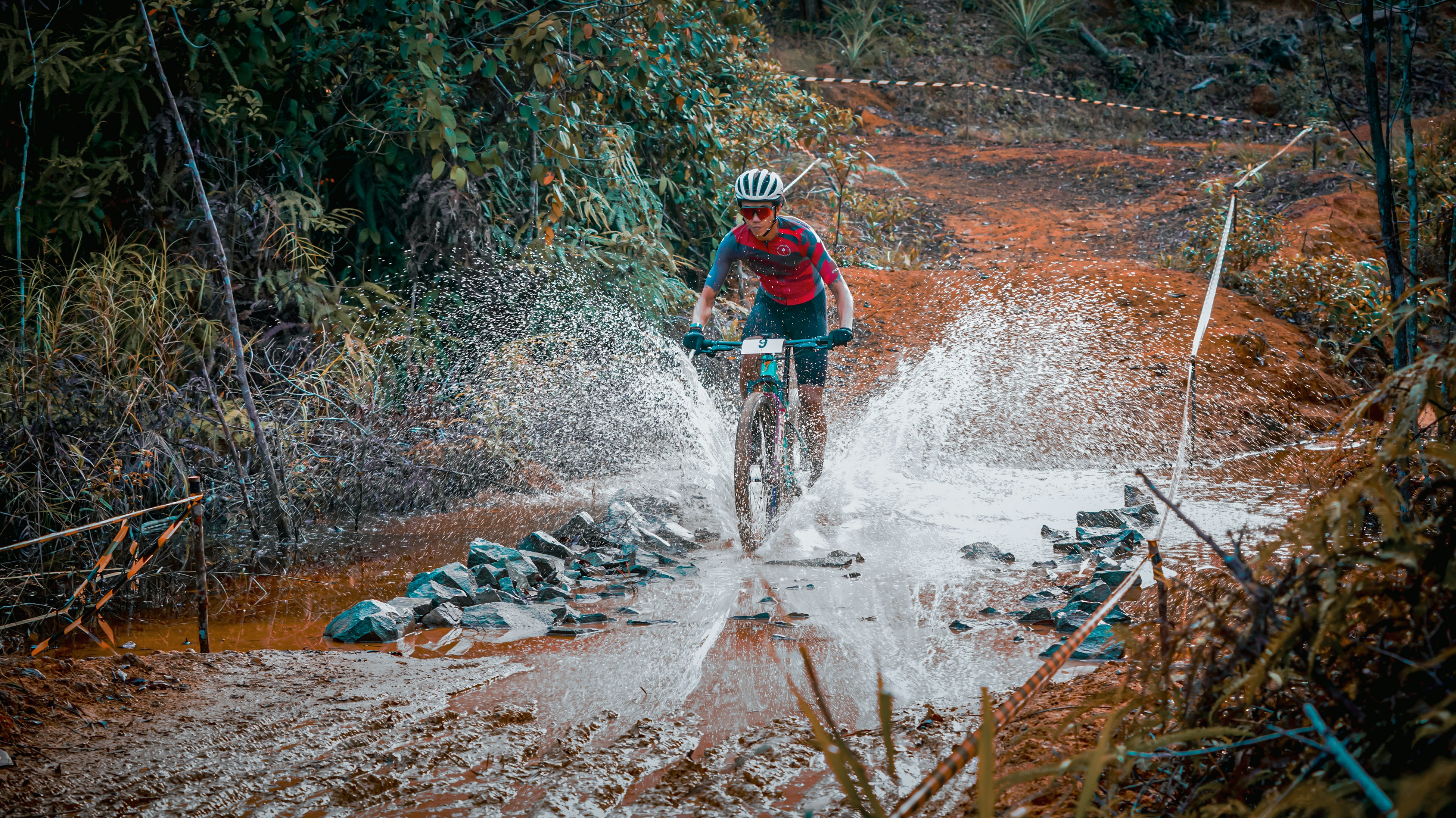 Cyclist splashes through muddy water on a trail.
