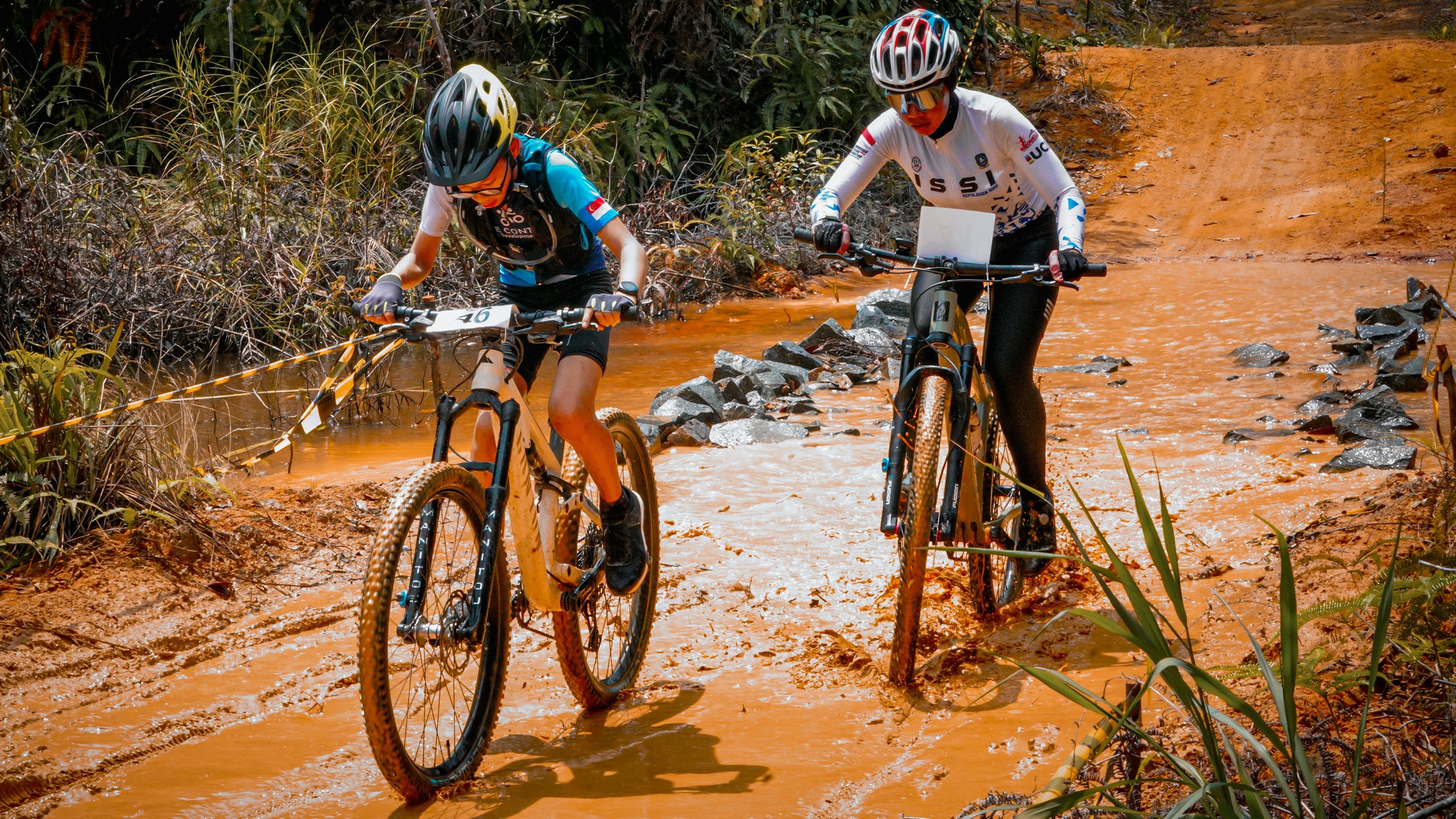 Two mountain bikers ride through a muddy trail.