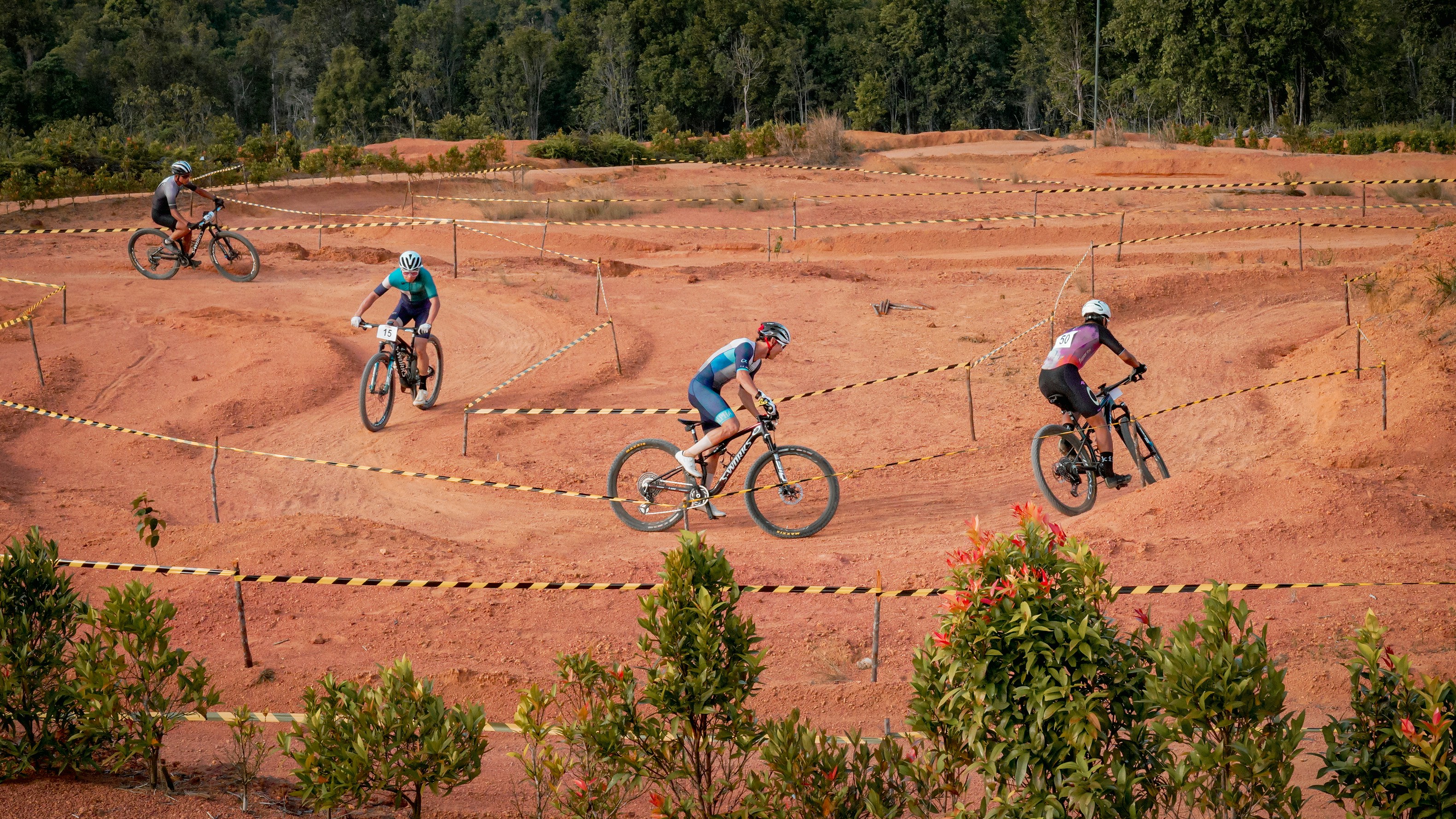 Cyclists race on a dirt track in the outdoors.