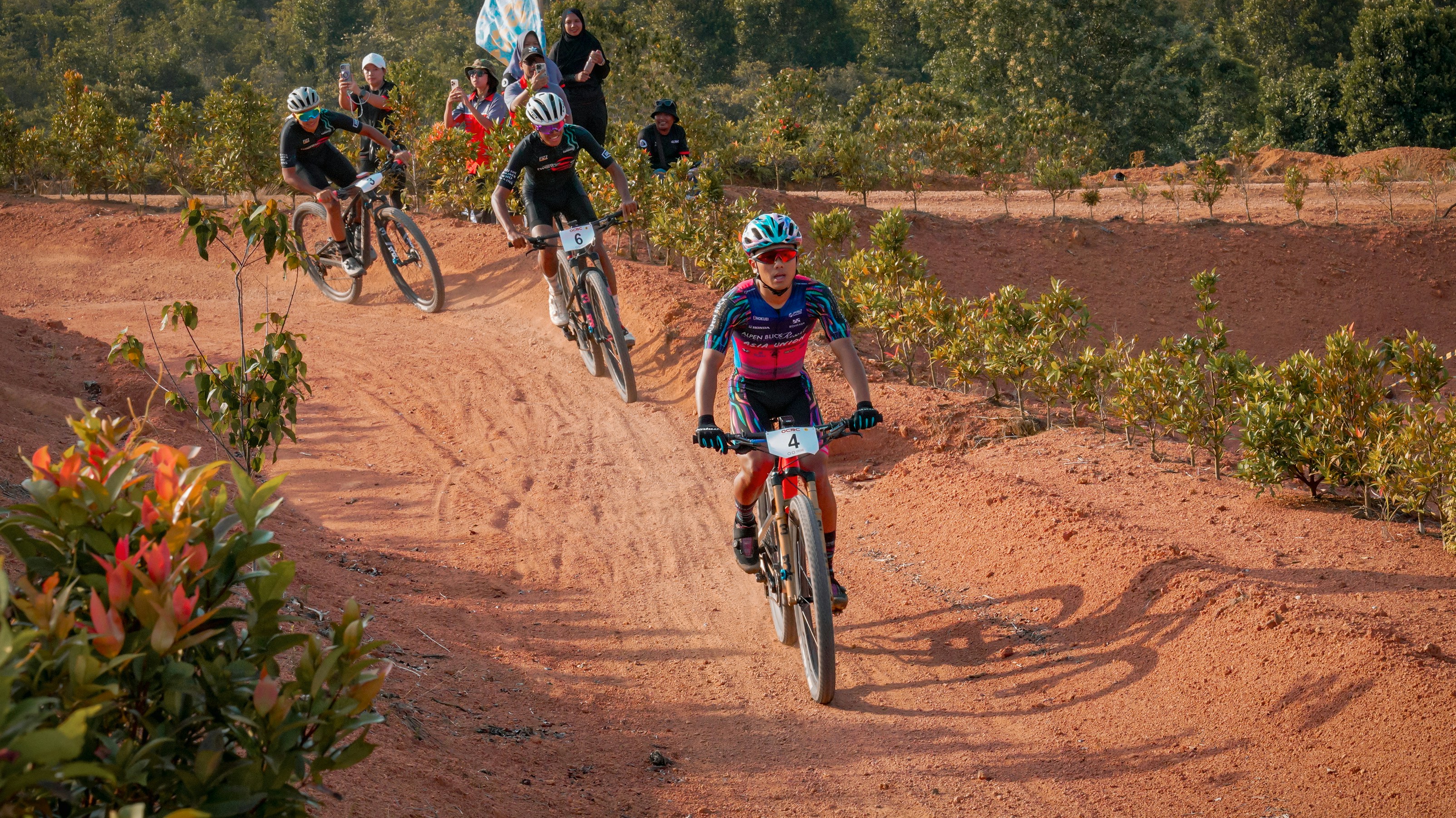 Mountain bikers race on a dirt track.