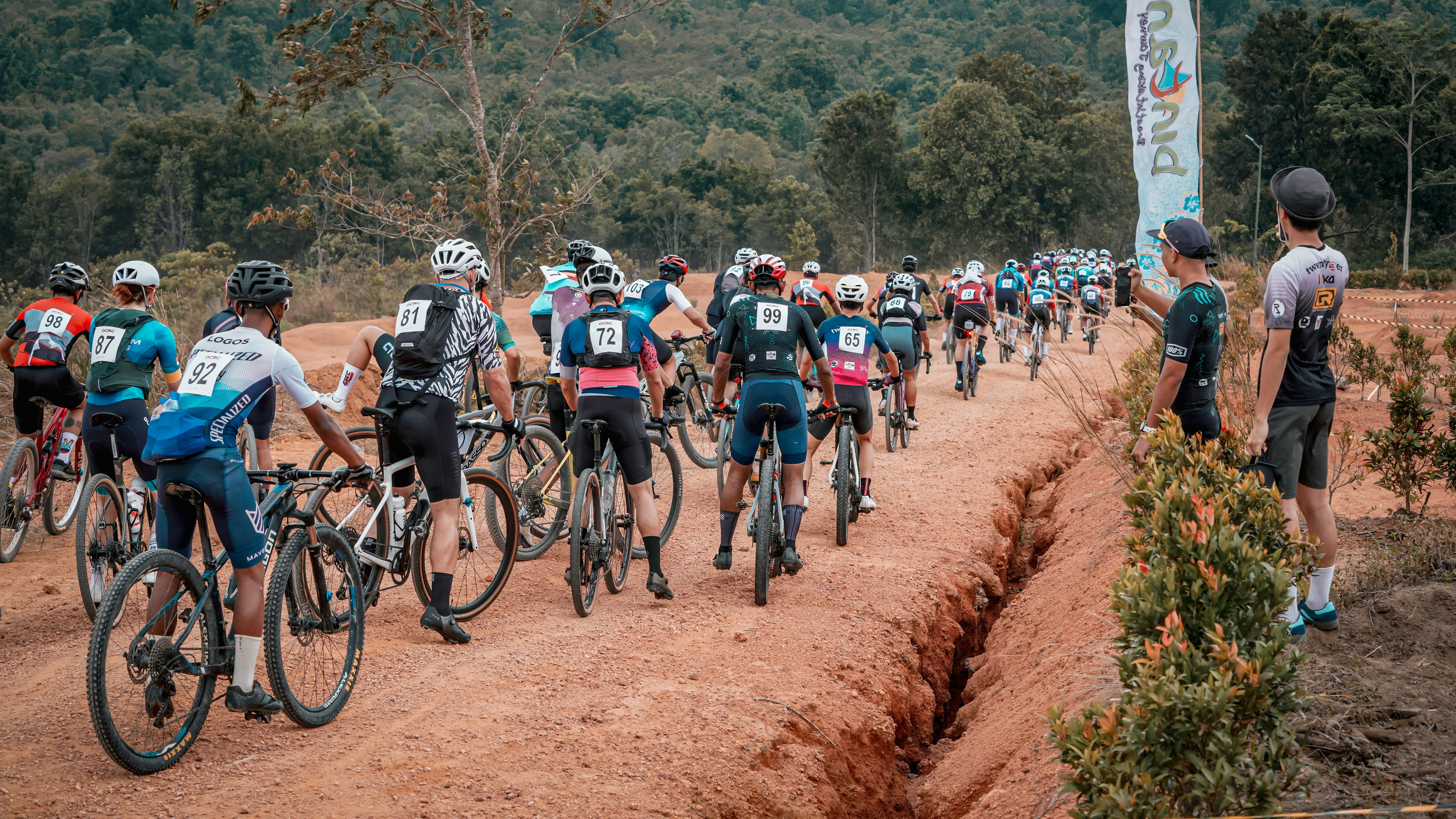 Cyclists race on a dirt track through the woods.