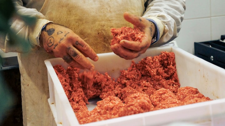 Butcher hands shaping ground meat on a work table, faceless overhead crop