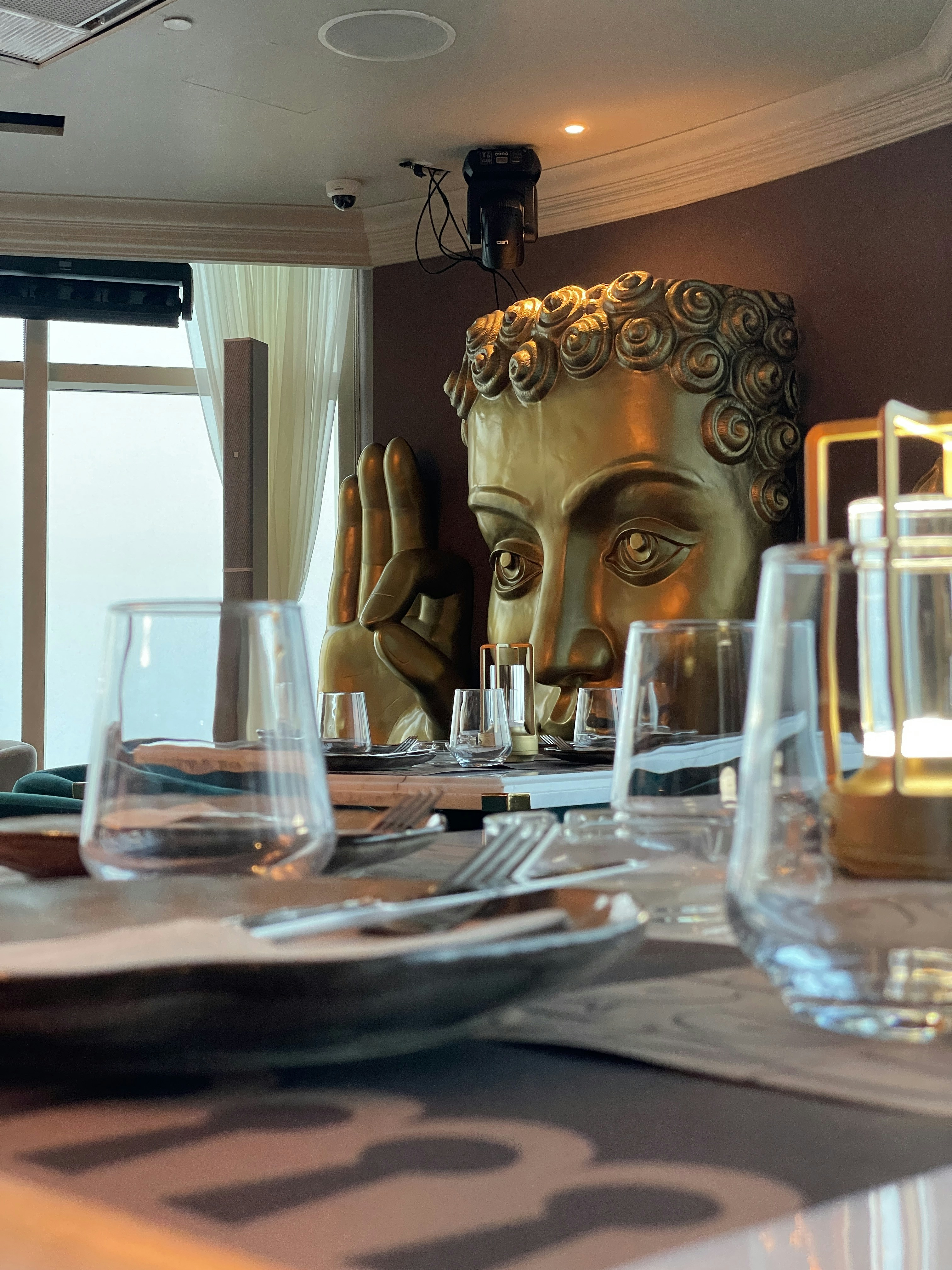 A golden buddha head stands over a dining table.