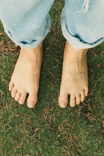 Bare feet stand on grass under jeans.