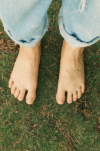 Bare feet stand on grass under jeans.