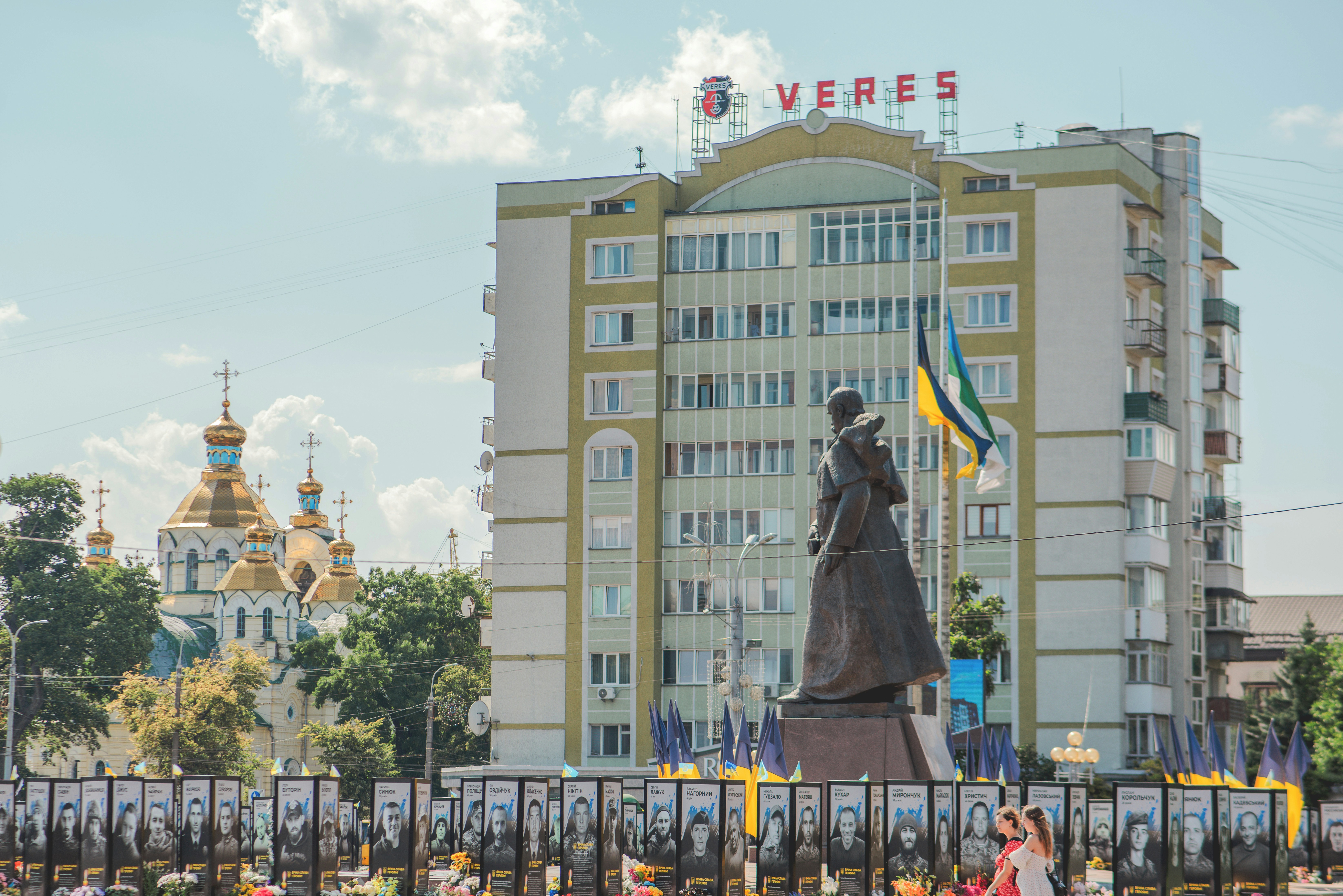 A city square features a statue and building