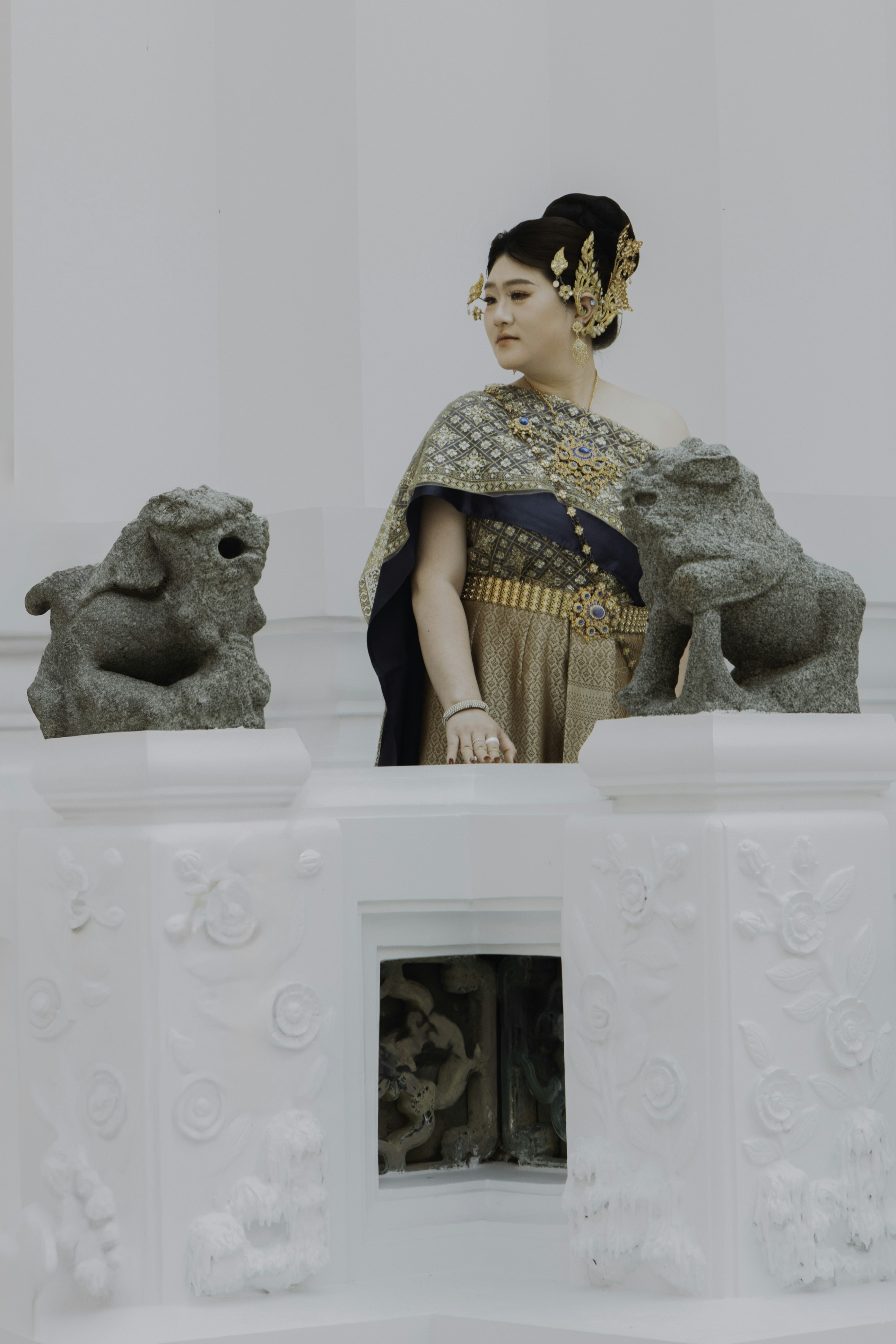 Una donna in abiti tradizionali tailandesi si trova tra due leoni di pietra.