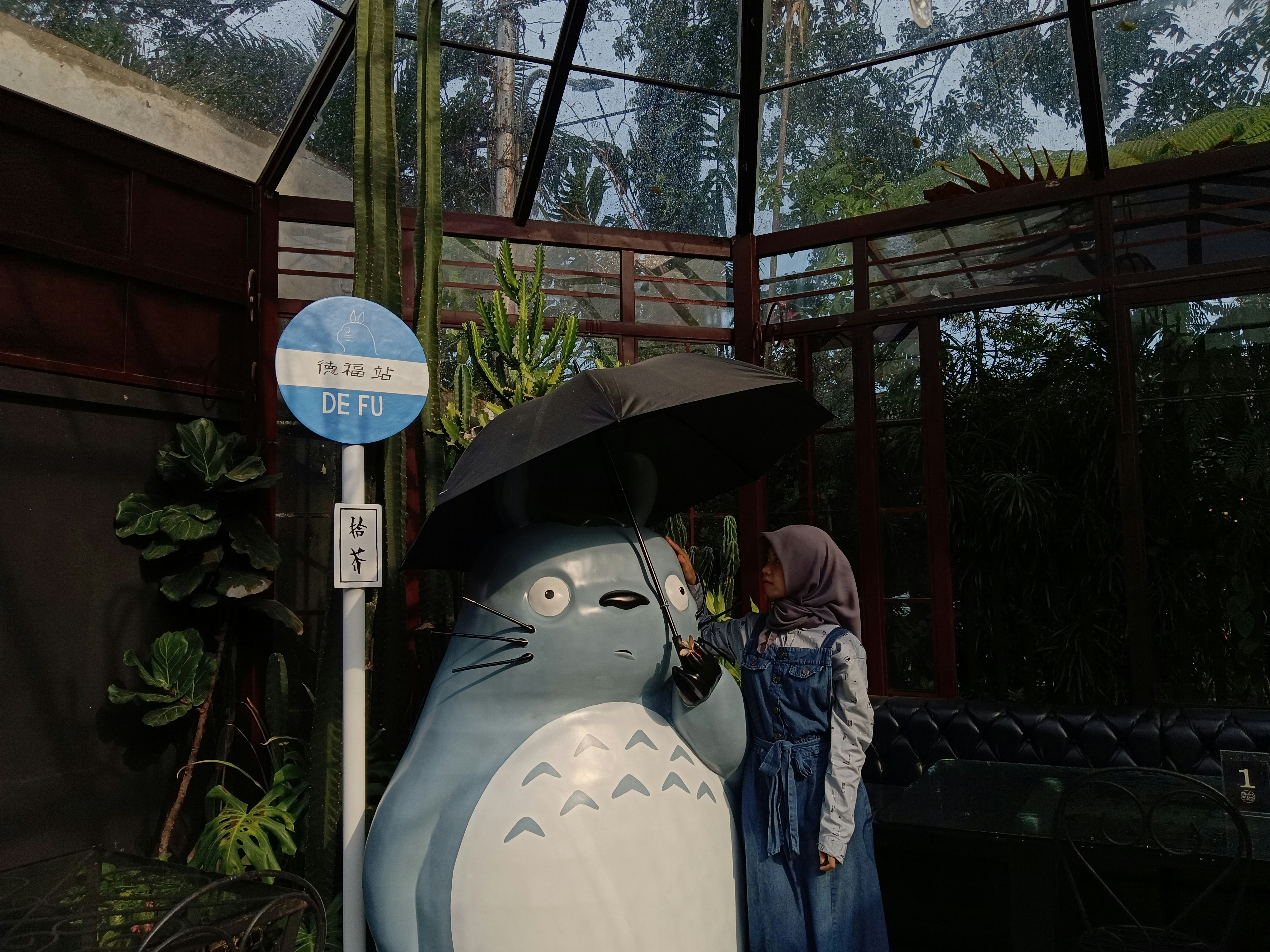 Seorang gadis berdiri di dekat totoro di bawah payung.