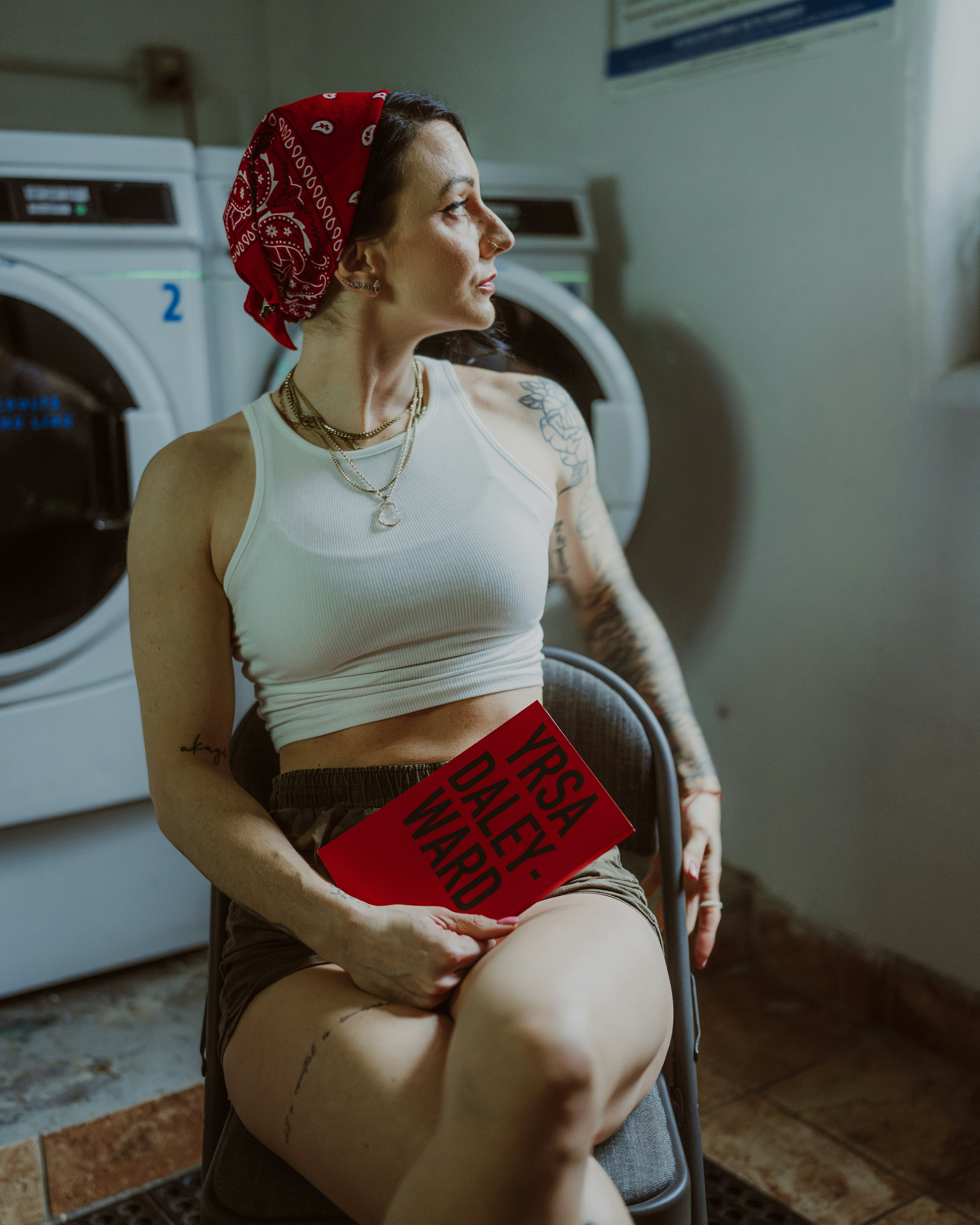 Woman with a book in a laundromat, looking away.