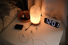 Nightstand with a lamp, clock, and chargers.