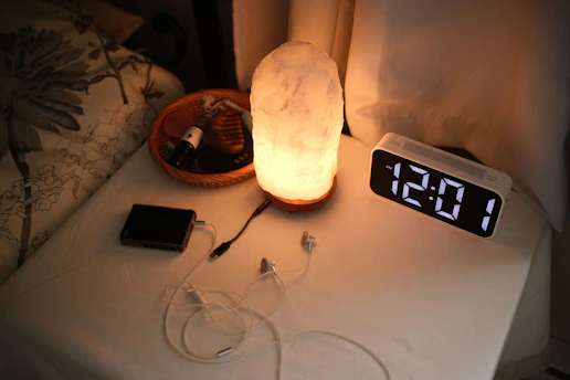 Nightstand with a lamp, clock, and chargers.