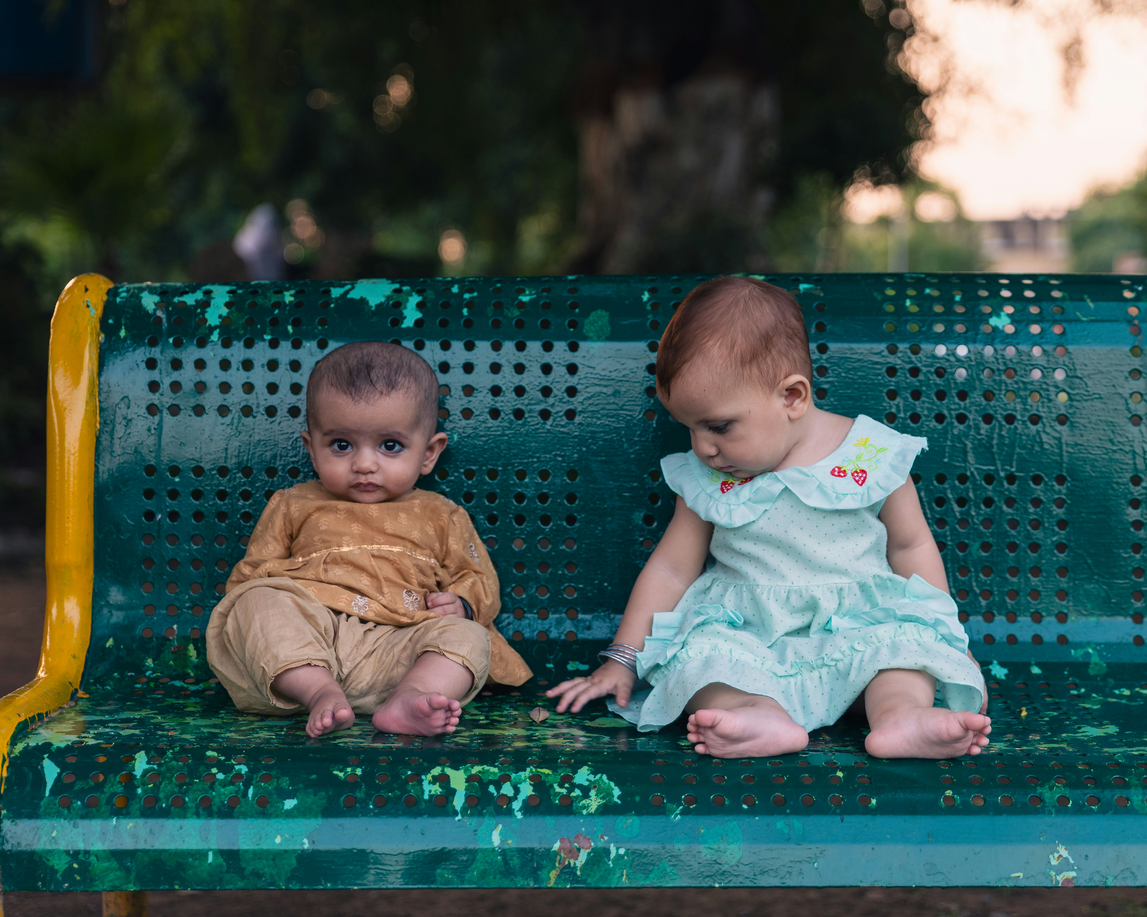 Two babies sitting on a green park bench