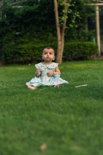 Baby sitting on green grass in a park.