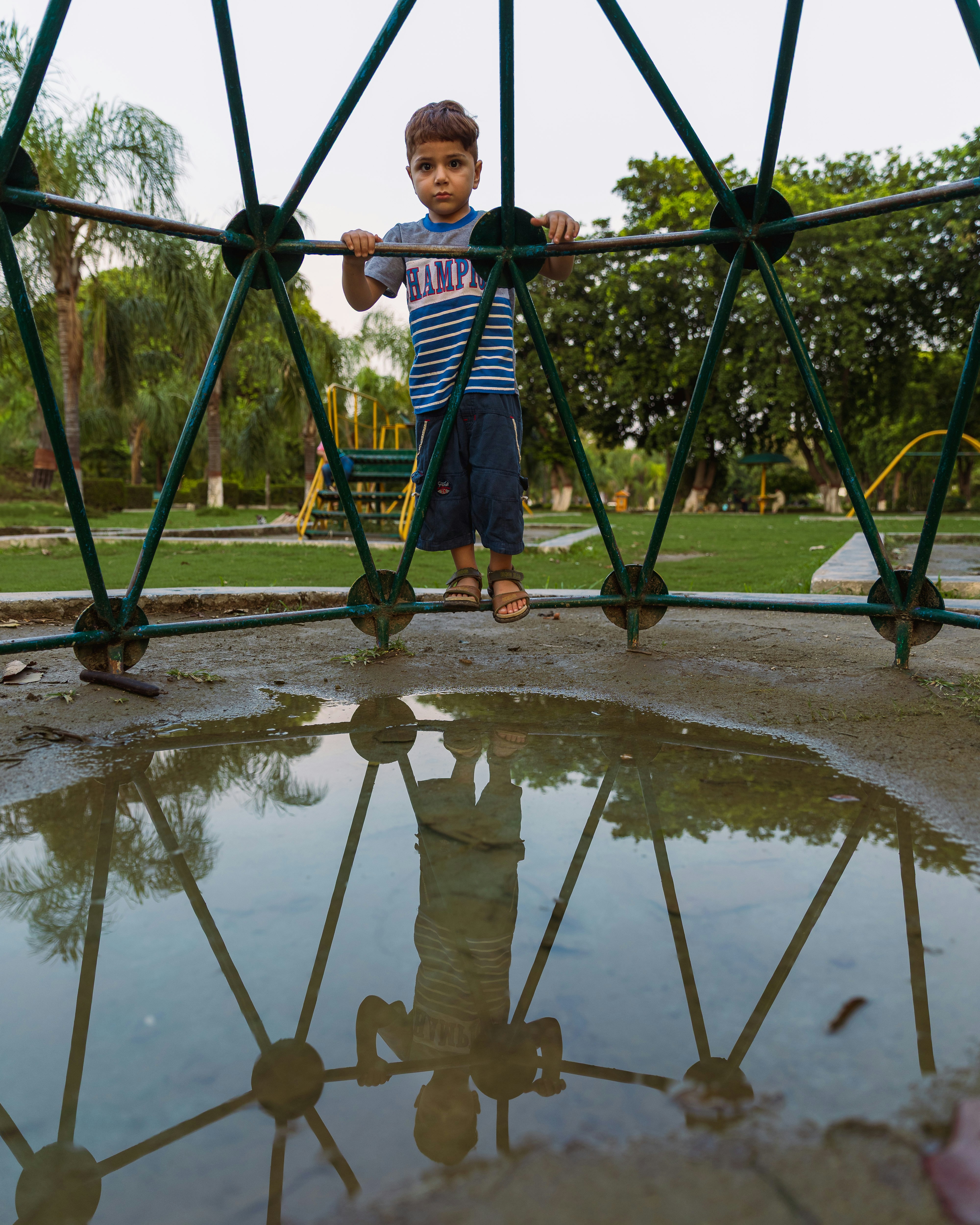 Junger Junge steht in der Nähe eines Klettergerüsts mit Reflexion