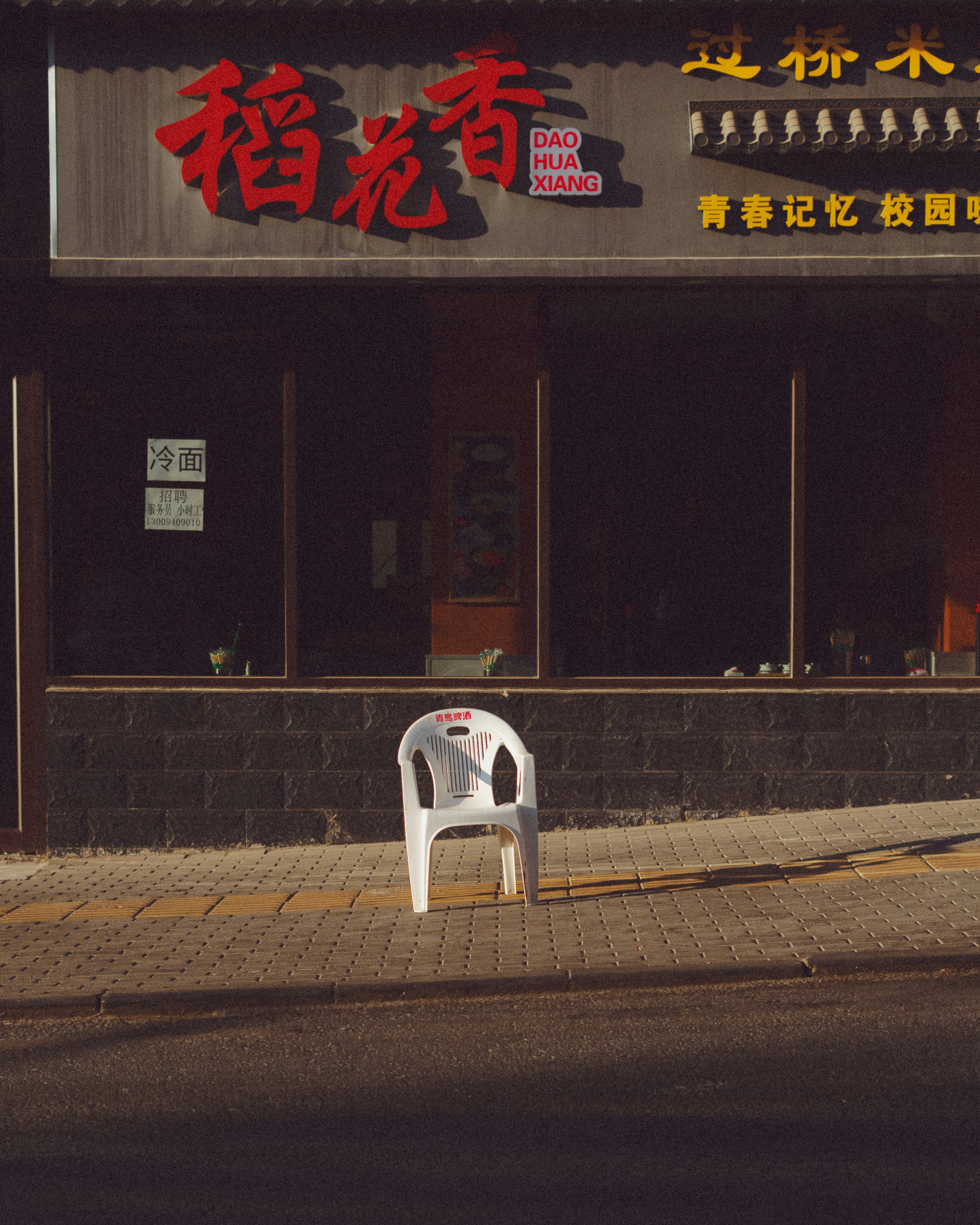 A white chair sits outside a storefront.