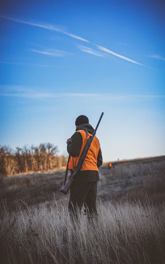 Hunter with shotgun in a field at sunset.