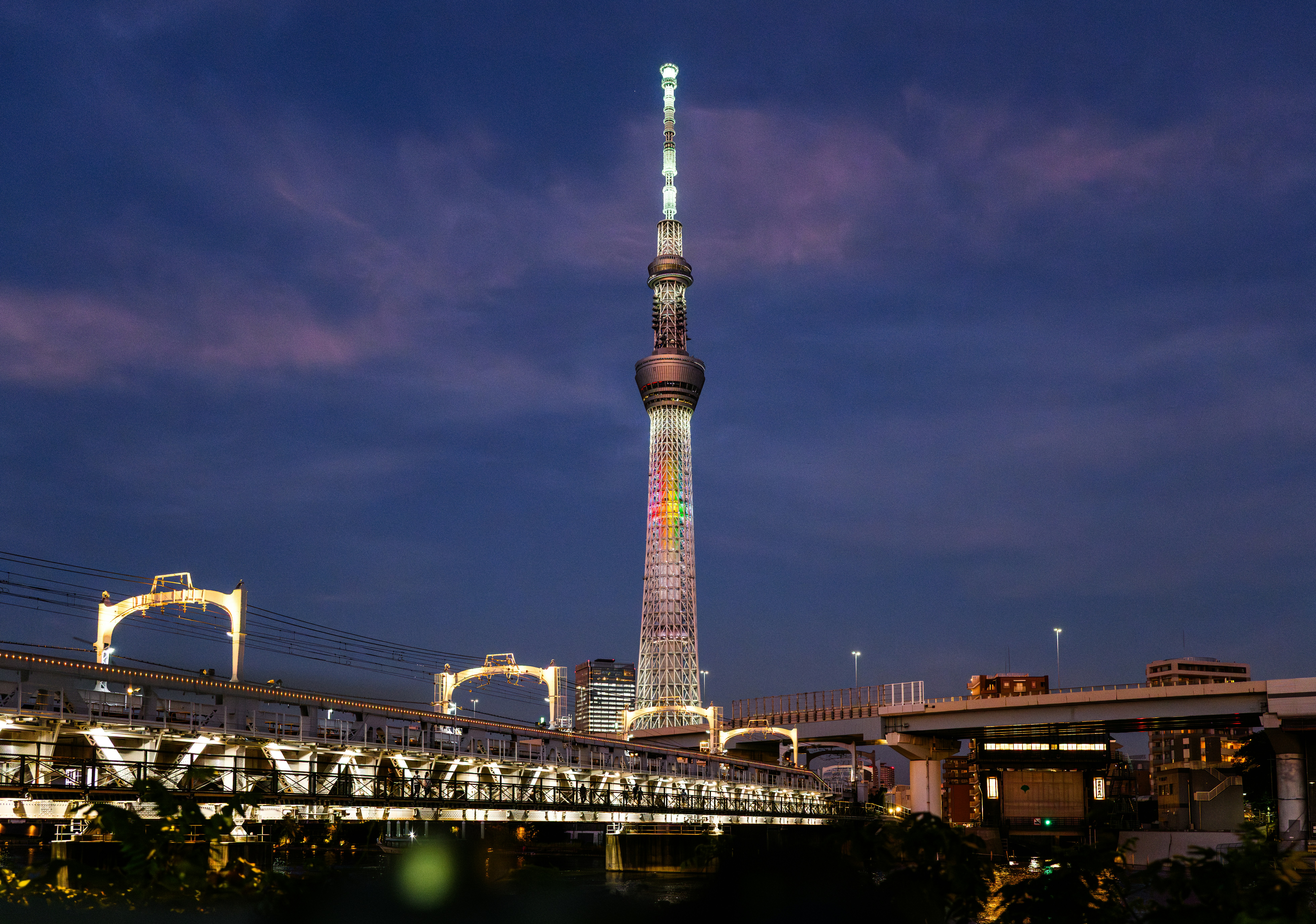Tall illuminated tower at dusk with bridge