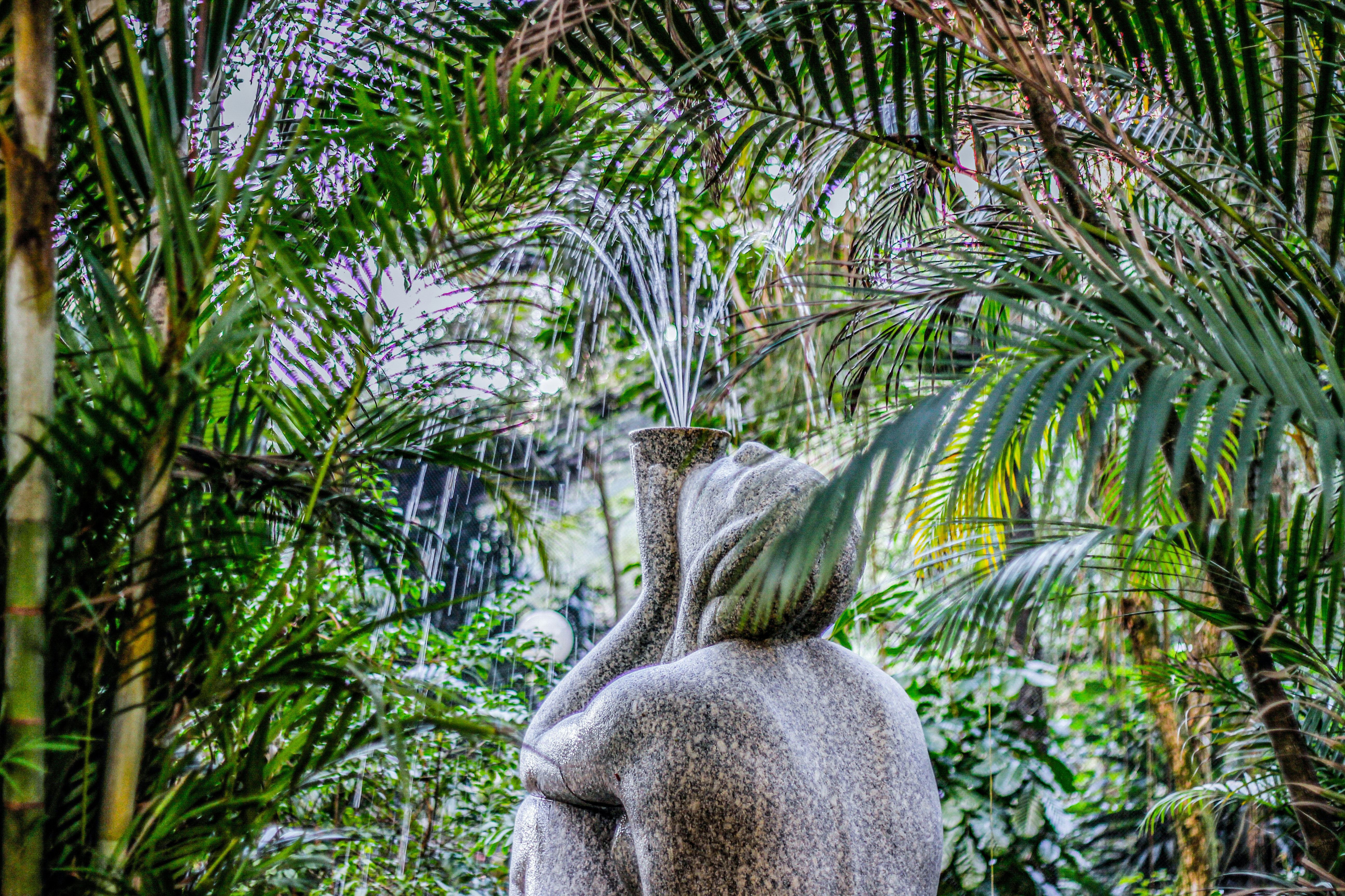 Stone statue with water fountain surrounded by lush greenery