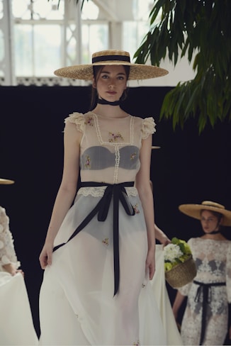 Woman in a wide-brimmed hat and sheer dress walks