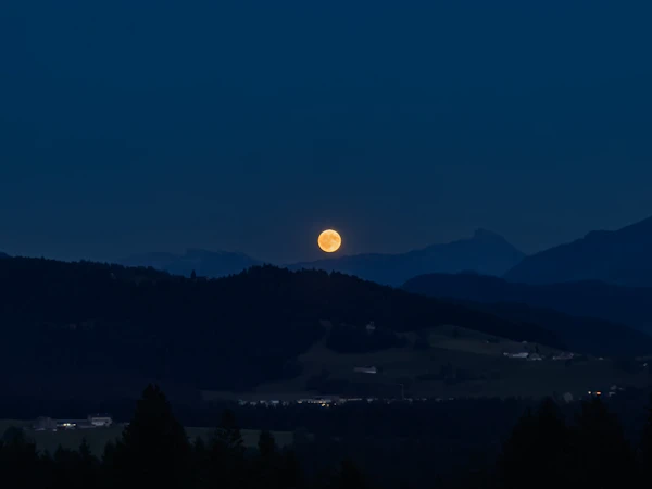 Full moon rising over a dark mountain landscape at night