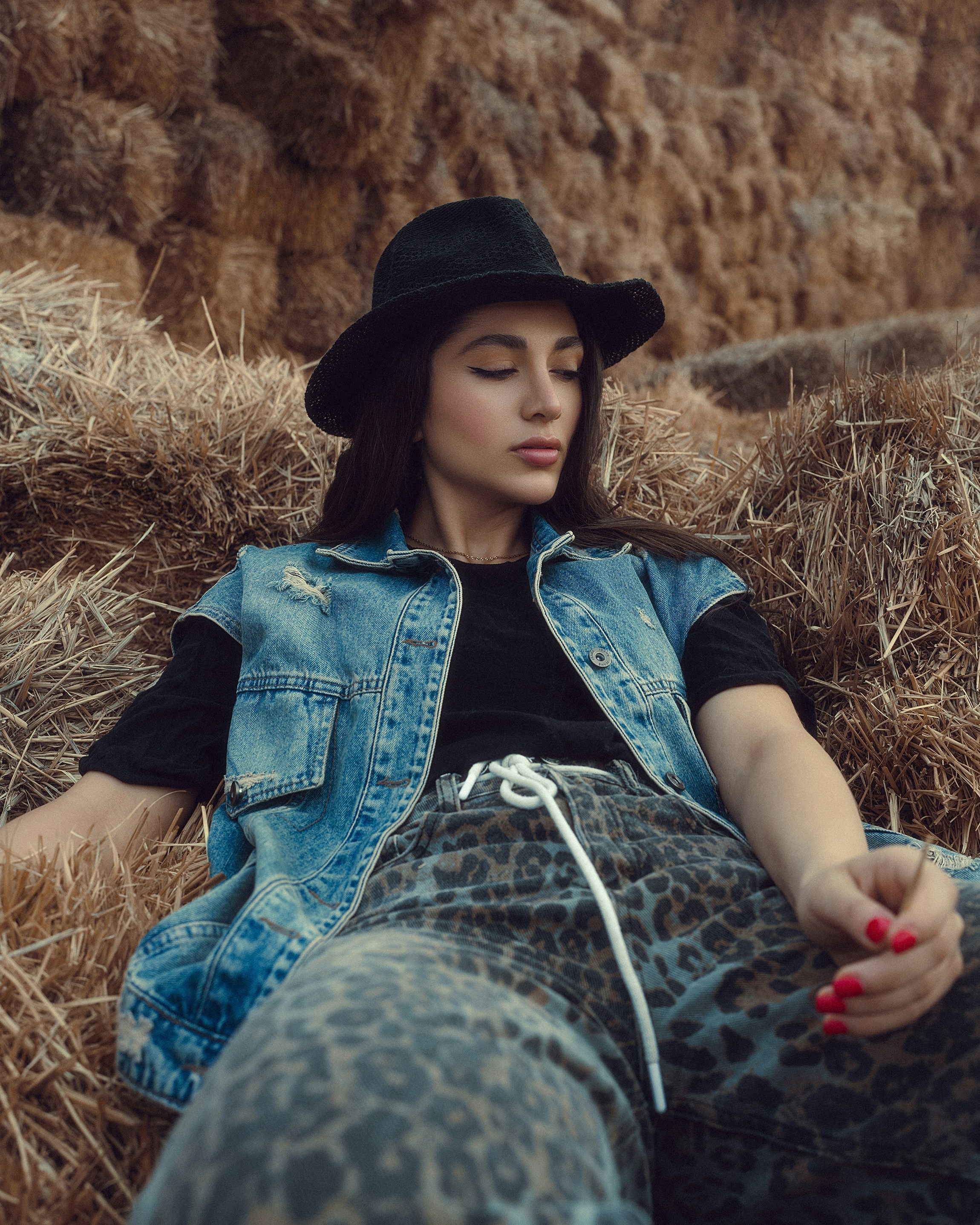 Femme au chapeau et gilet en jean reposant sur le foin