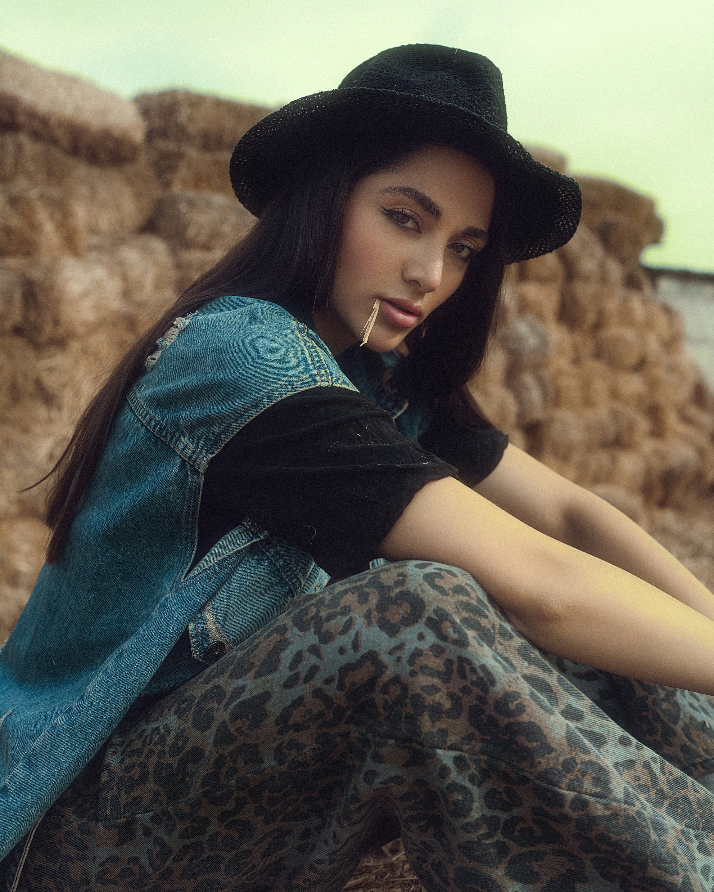 Une jeune femme en chapeau et gilet en jean est assise près de balles de foin