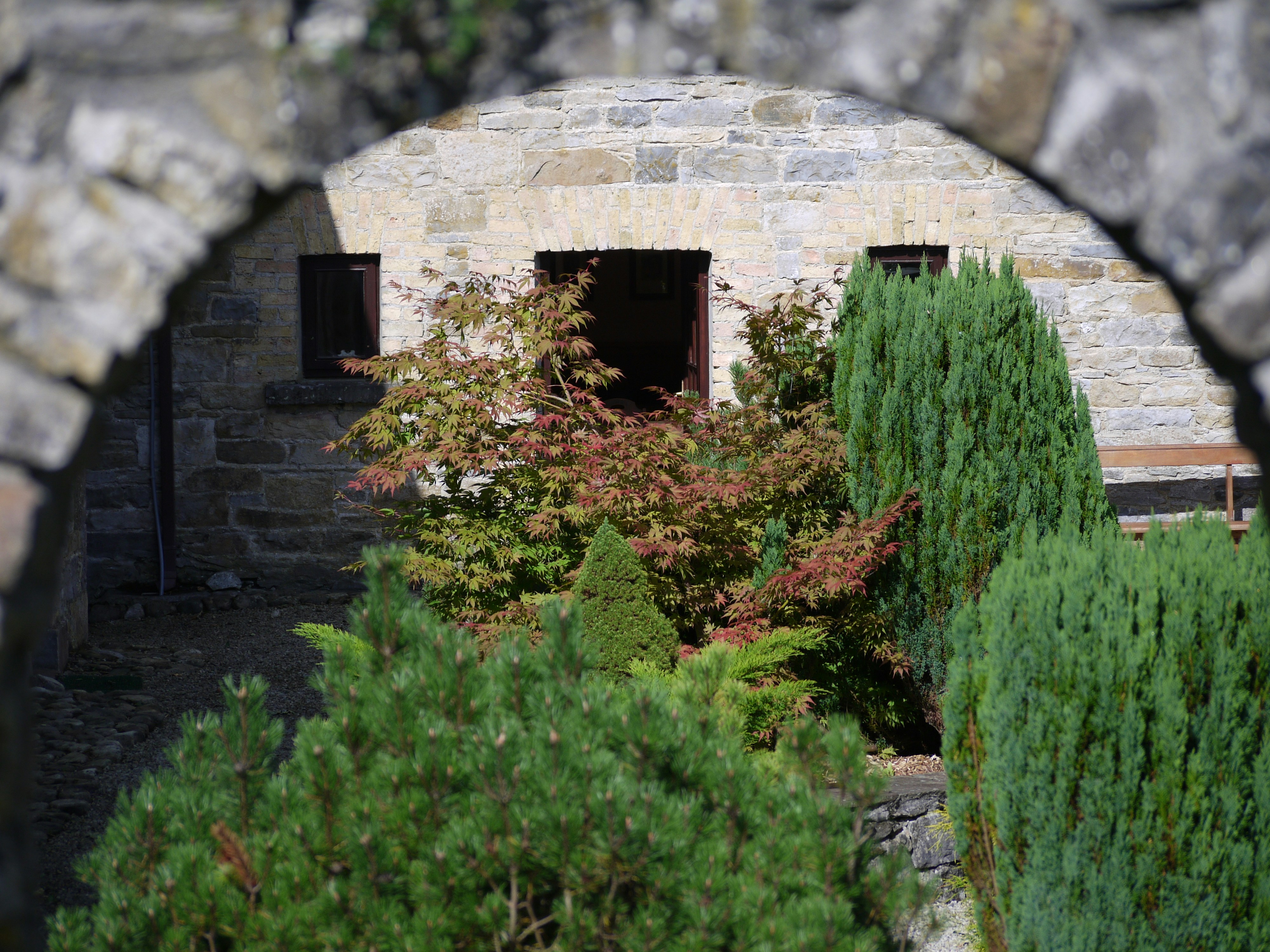 Stone archway with greenery and a small building.