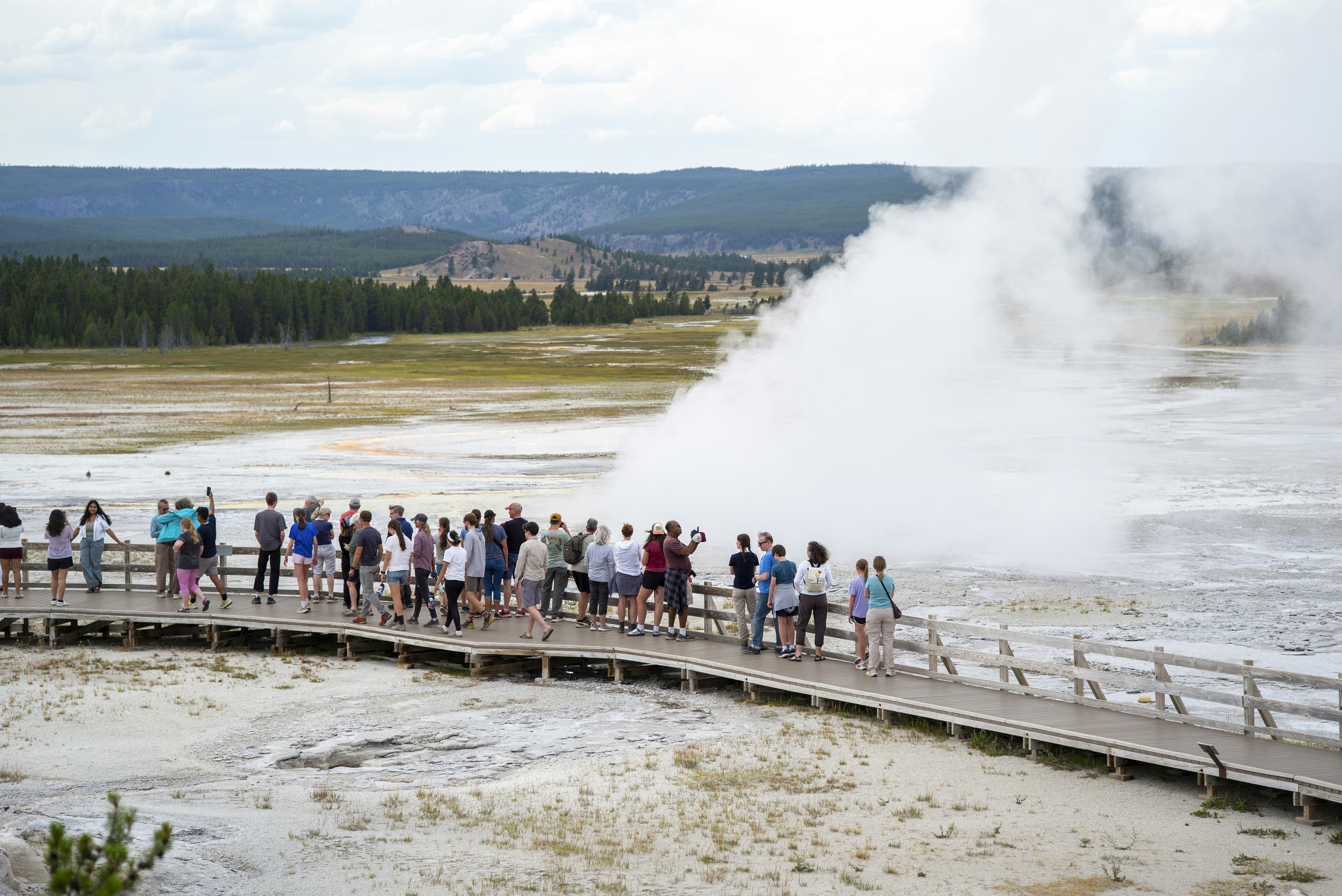 Geyser erupting as visitors gather along the boardwalk in Yellowstone National Park