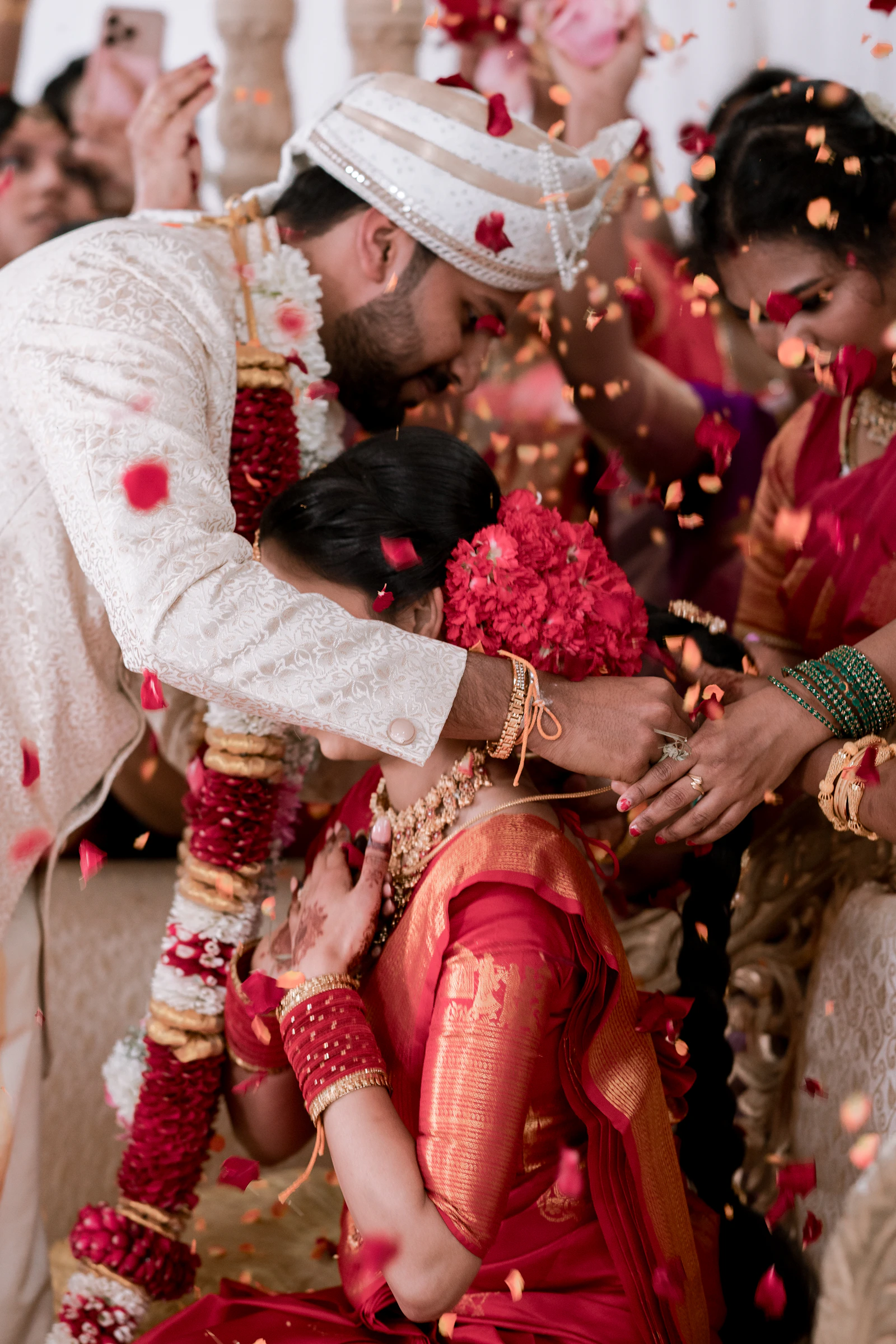A couple exchanging garlands as guests throw petals.