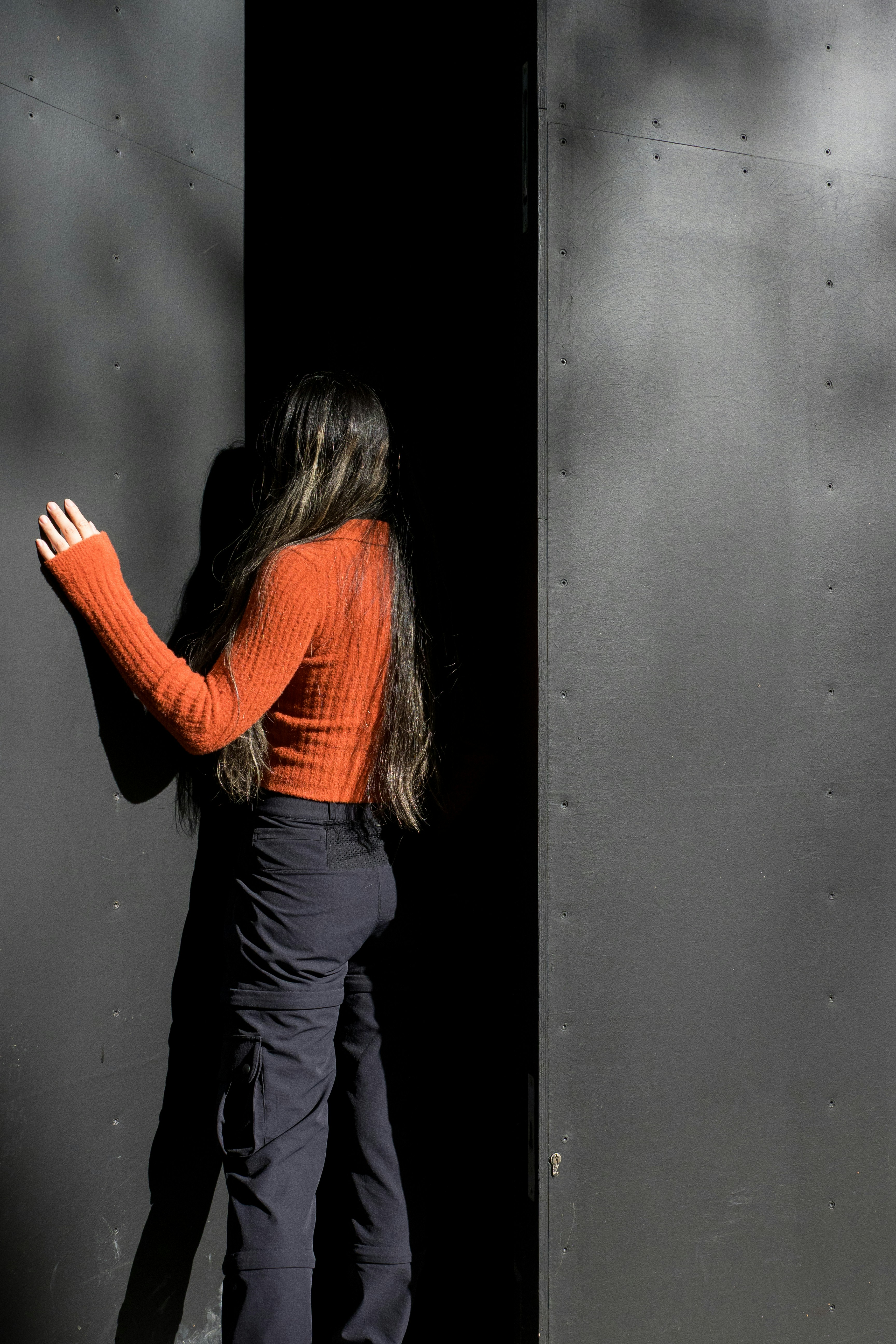 Woman in orange sweater reaching into dark doorway