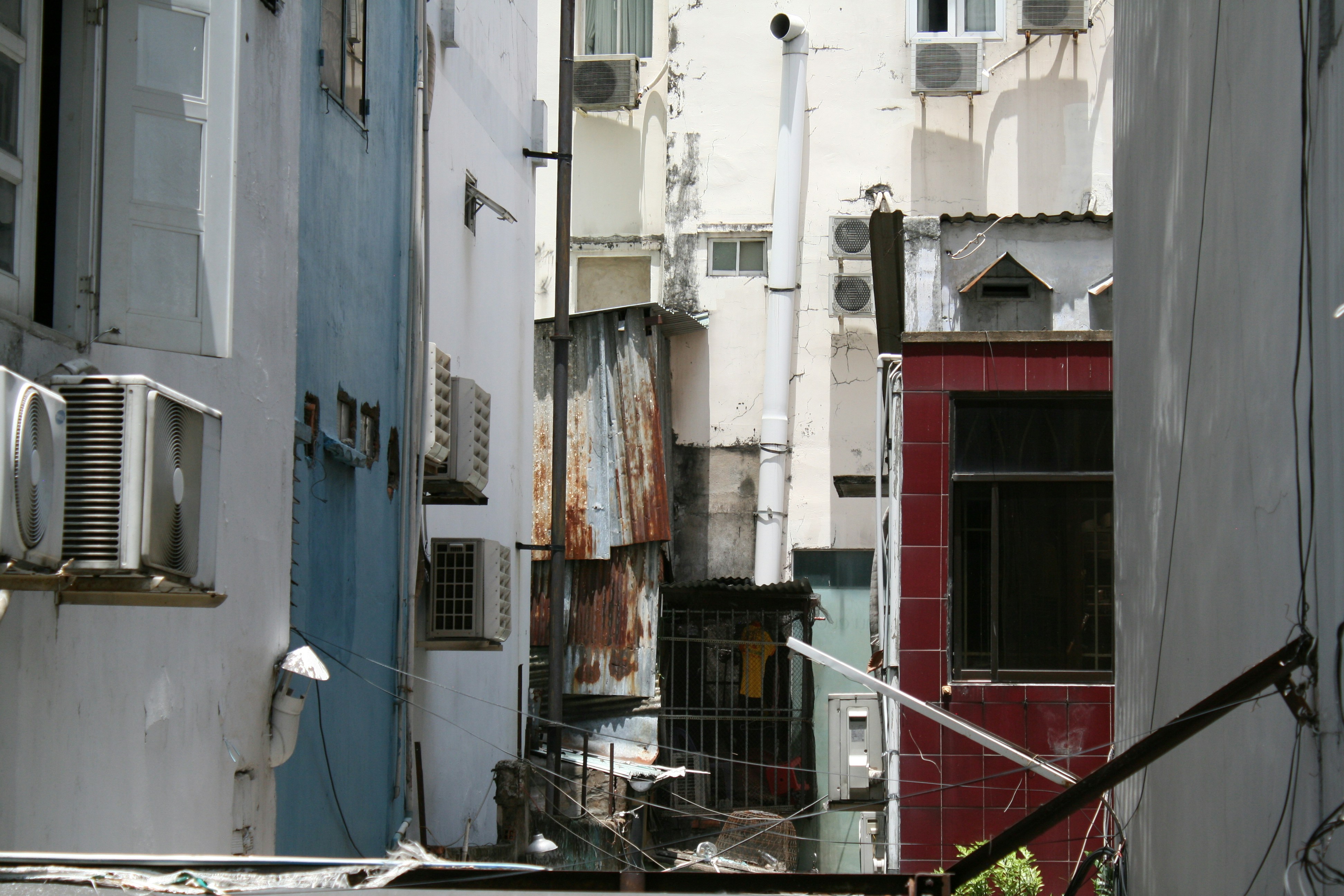 Narrow alleyway between buildings with air conditioning units.