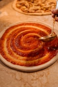 Sauce being spread on pizza dough in a spiral.