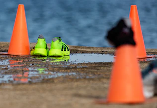 Neon green running shoes near orange cones by water