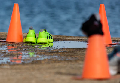 Neon green running shoes near orange cones by water