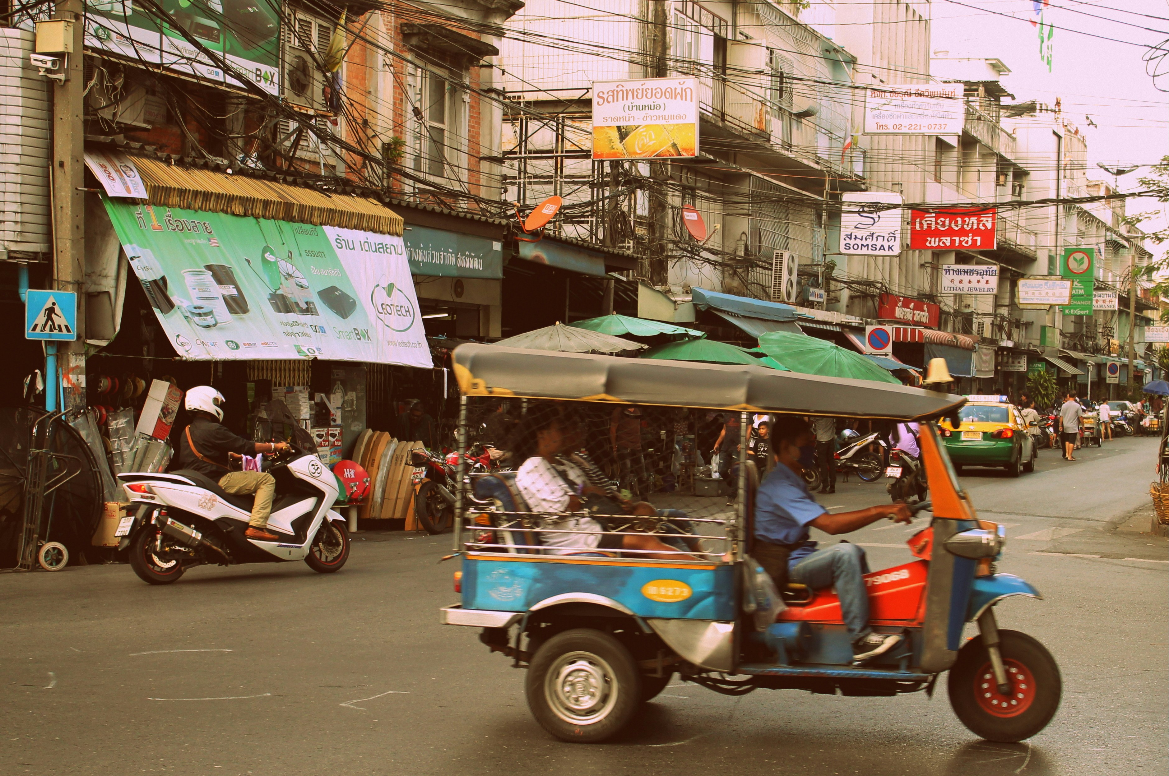 Tuk-tuk driving down a busy street with shops.
